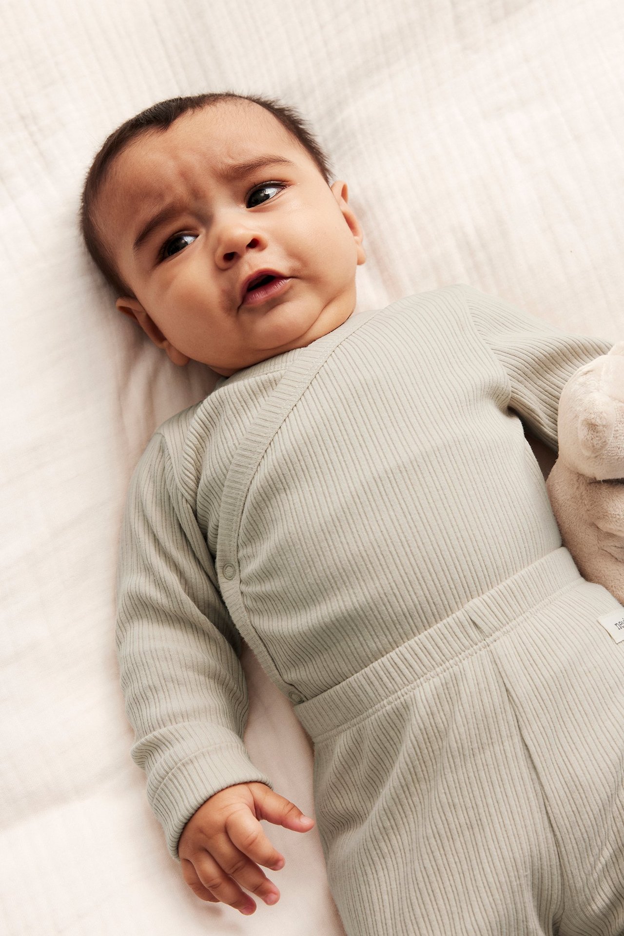 Närbild på en baby i en beige ribbad omlottbody med tryckknappar och matchande byxor.