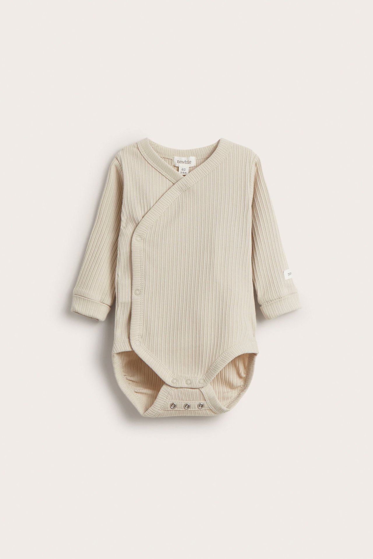 Frontvy av en beige ribbad långärmad omlottbody för baby med tryckknappar i grenen.