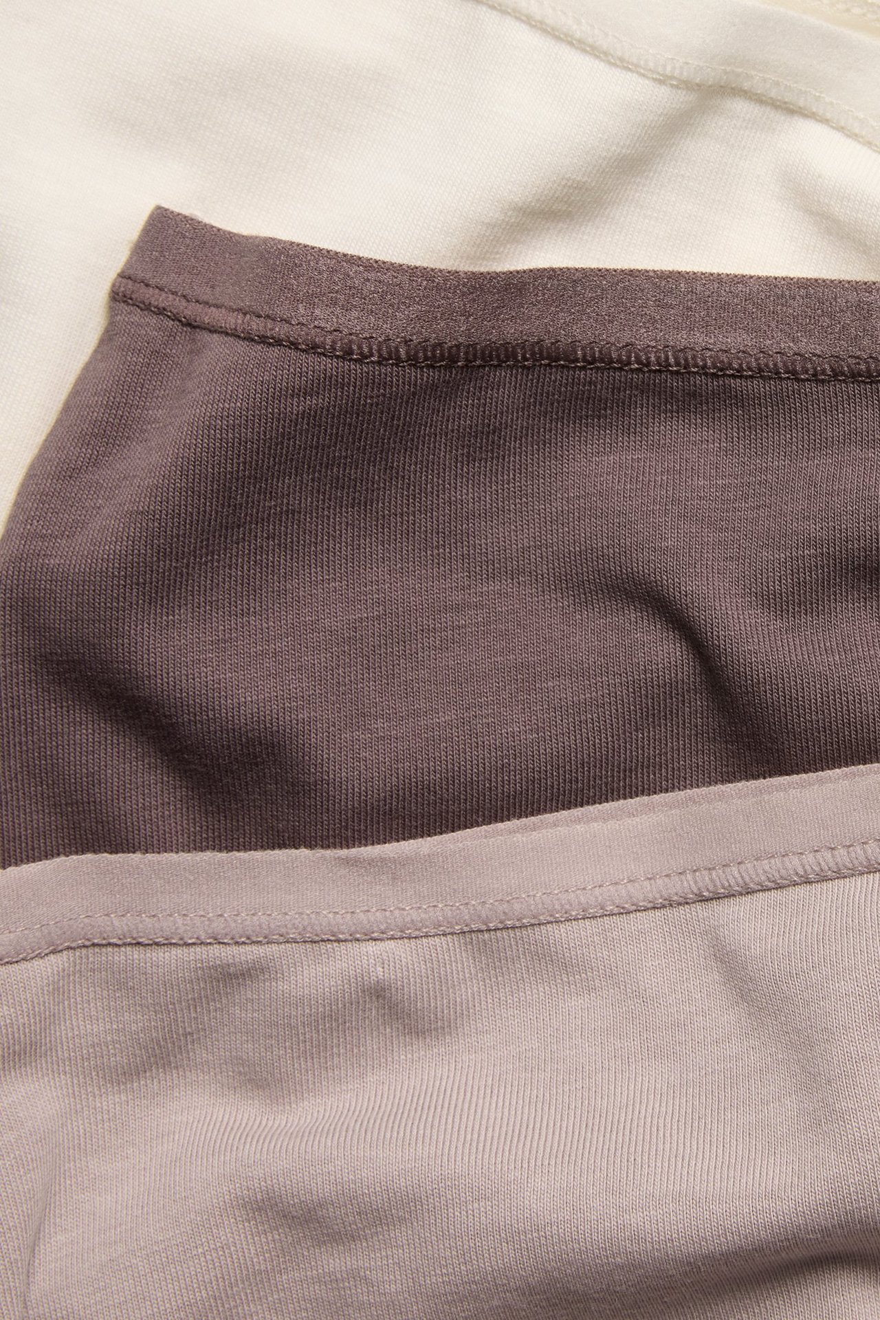 Nærbilde av tre ensfargede bomullstruser: plomme, lys grå og kremhvit.