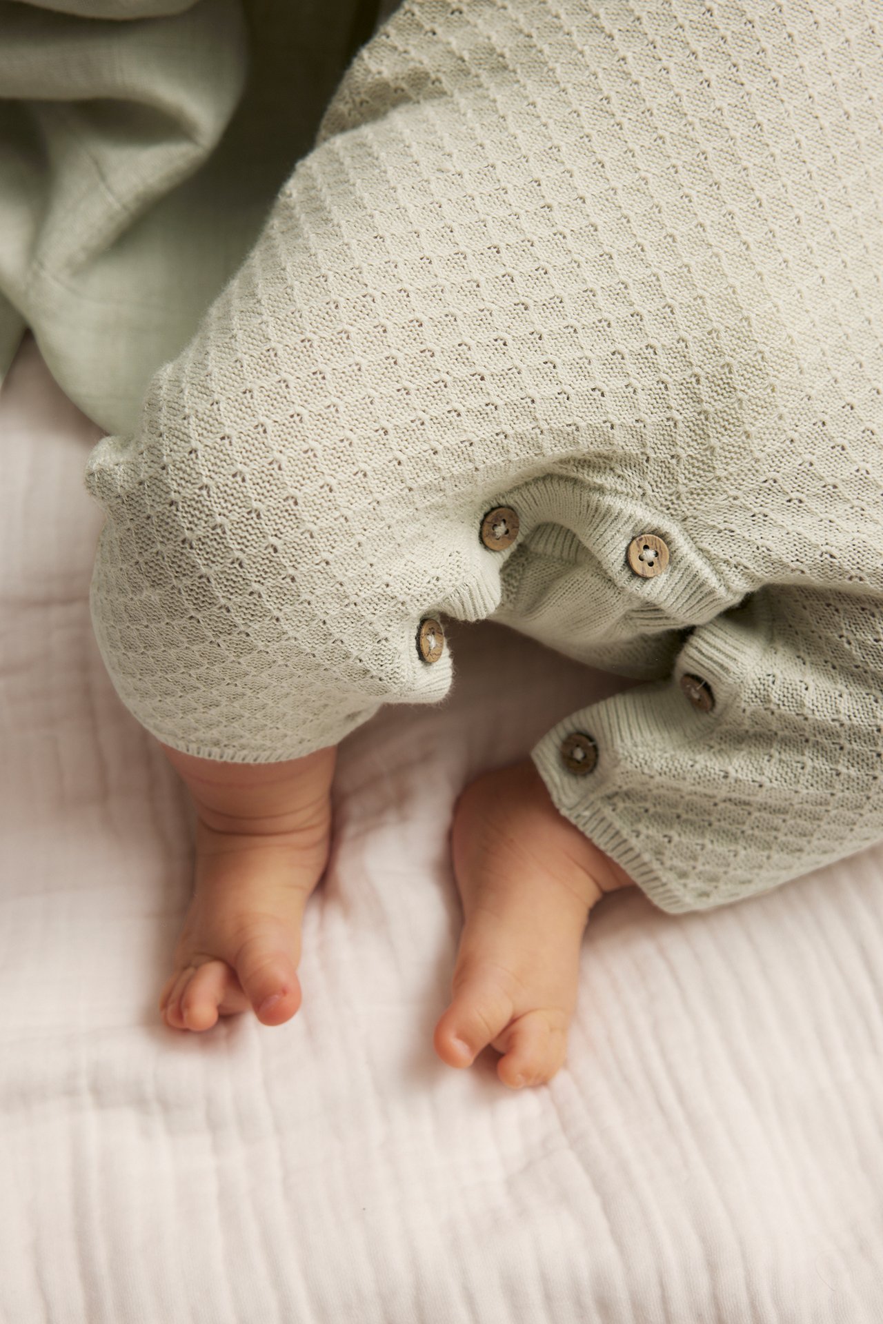 Nærbilde av en baby i lysegrønn strikket bomullsjumpsuit med treknapper.