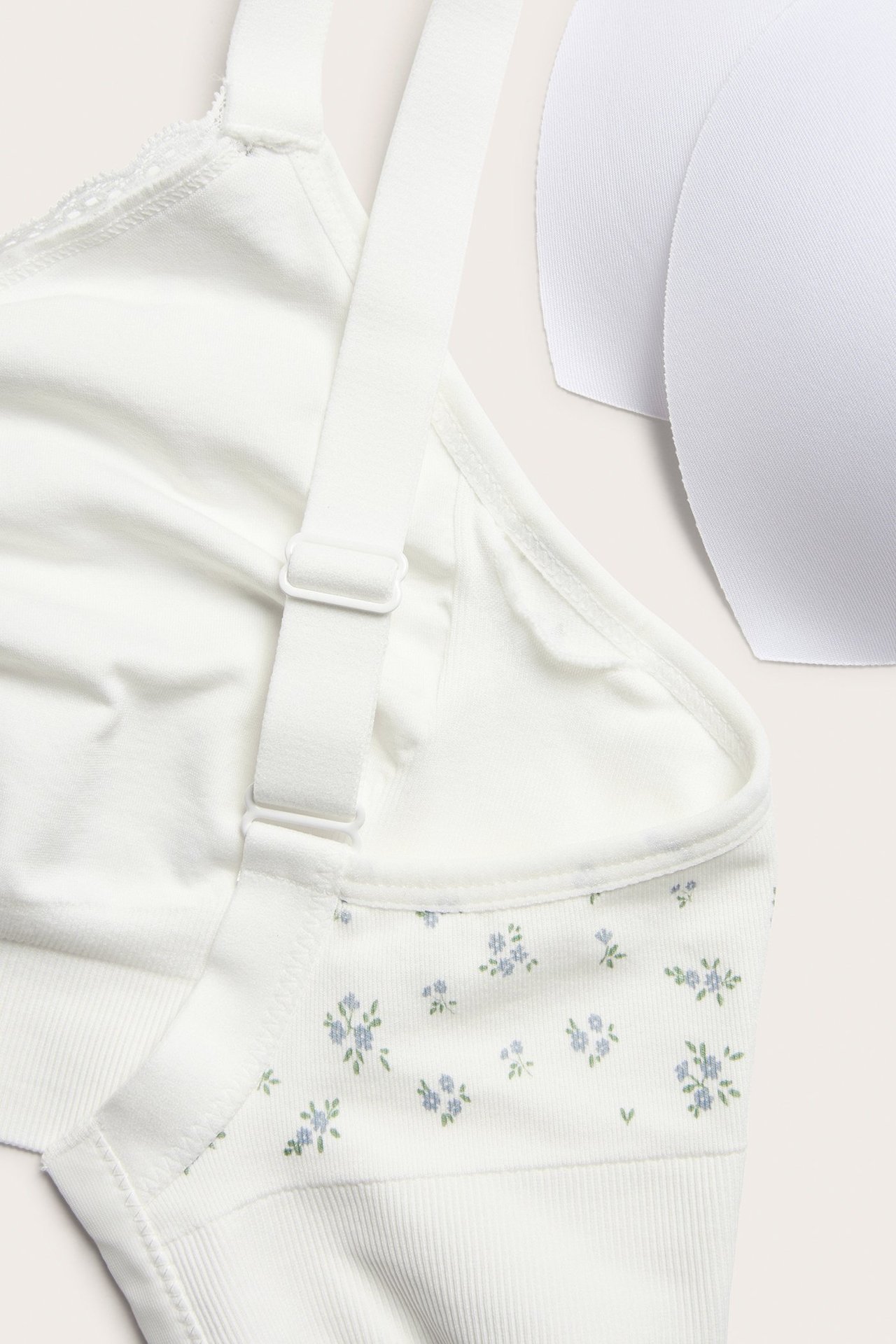 Zbliżenie: Ecru bezszwowy biustonosz bez fiszbin z niebieskim kwiatowym wzorem, regulowane ramiączka i dwa białe pady.