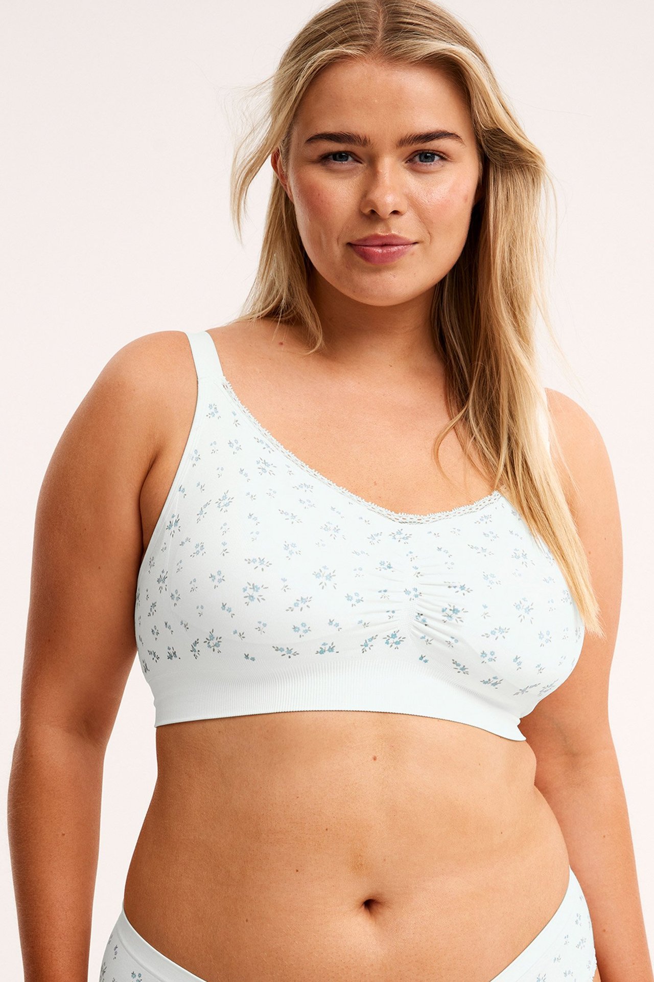 Widok z przodu: Kobieta w kremowym, bezszwowym biustonoszu bez fiszbin z niebieskim kwiatowym wzorem, marszczeniem i majtkami.