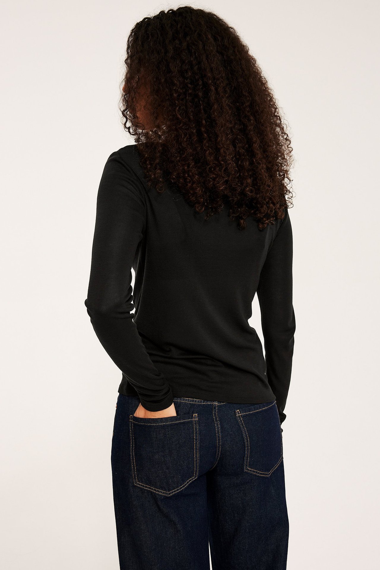 Ryggbilde av en kvinne i en tettsittende svart lyocell-langermet topp og mørkeblå jeans.