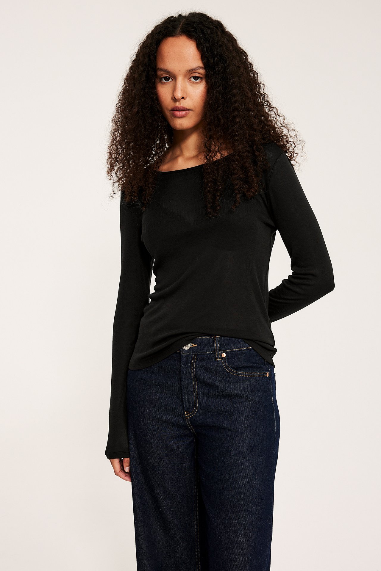 Forfra, kvinne i svart langermet lyocell-topp og mørkeblå jeans.