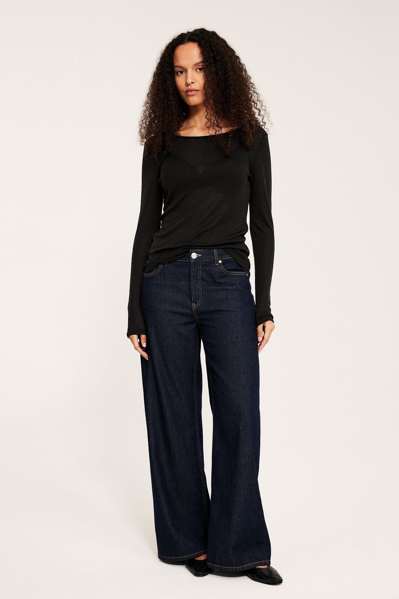 Frontvisning: Kvinne i svart langermet lyocelltopp, mørkeblå vide jeans og svarte flate sko.
