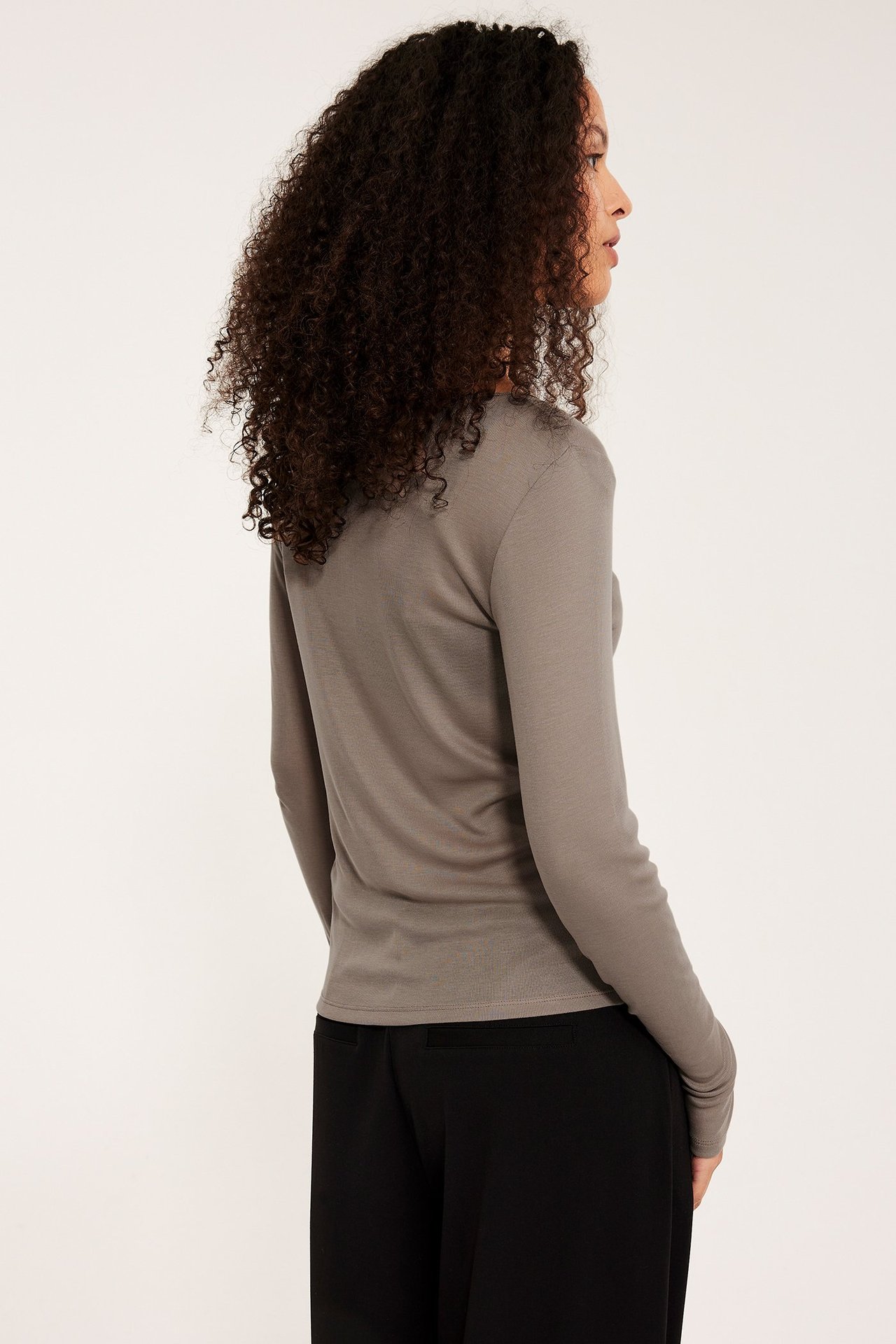 Widok z boku kobiety w ciemnobeżowym topie z długim rękawem i czarnych spodniach.