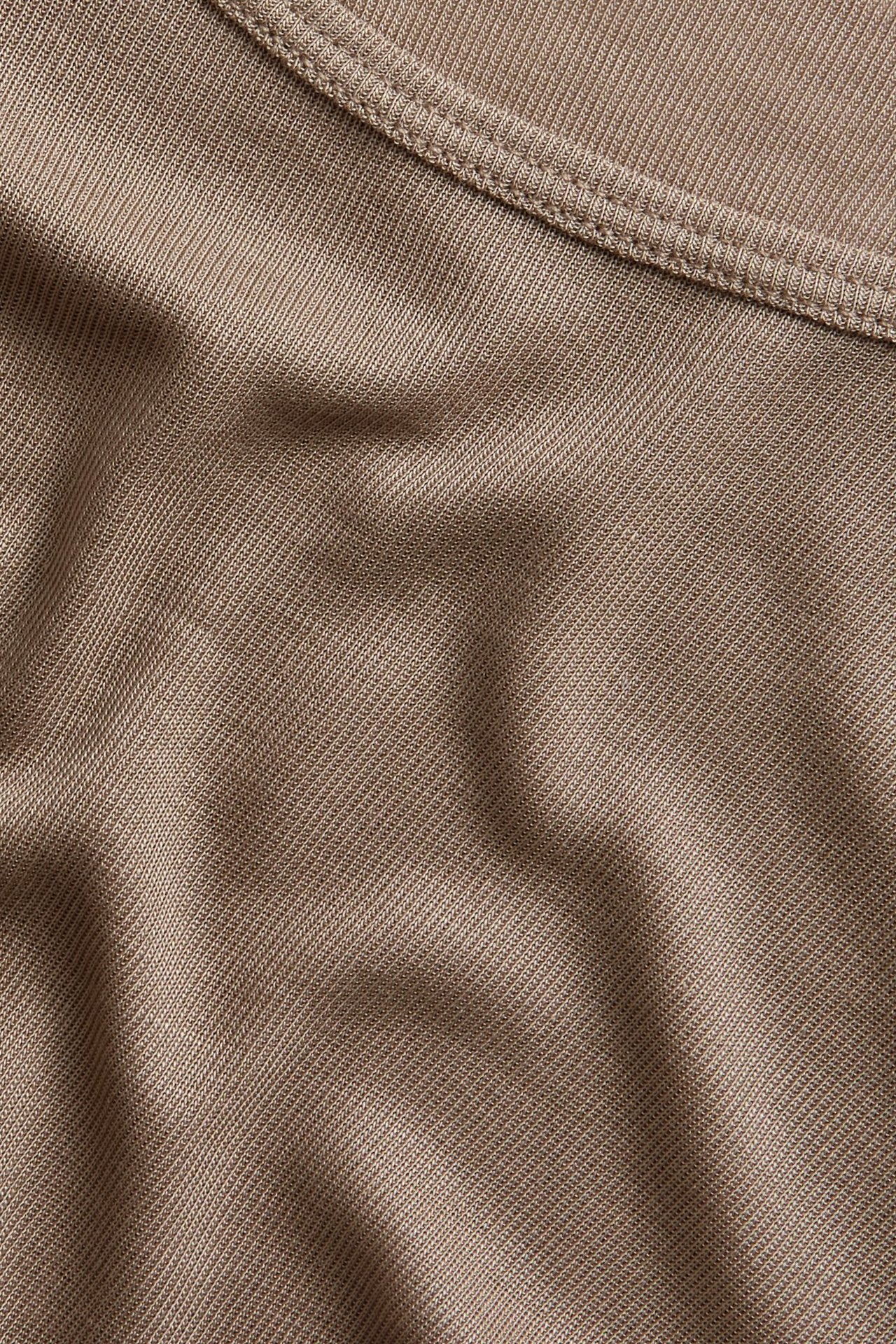 Zbliżenie na ciemnobeżowy, jednolity top z długim rękawem z lyocellu z widocznym szwem.