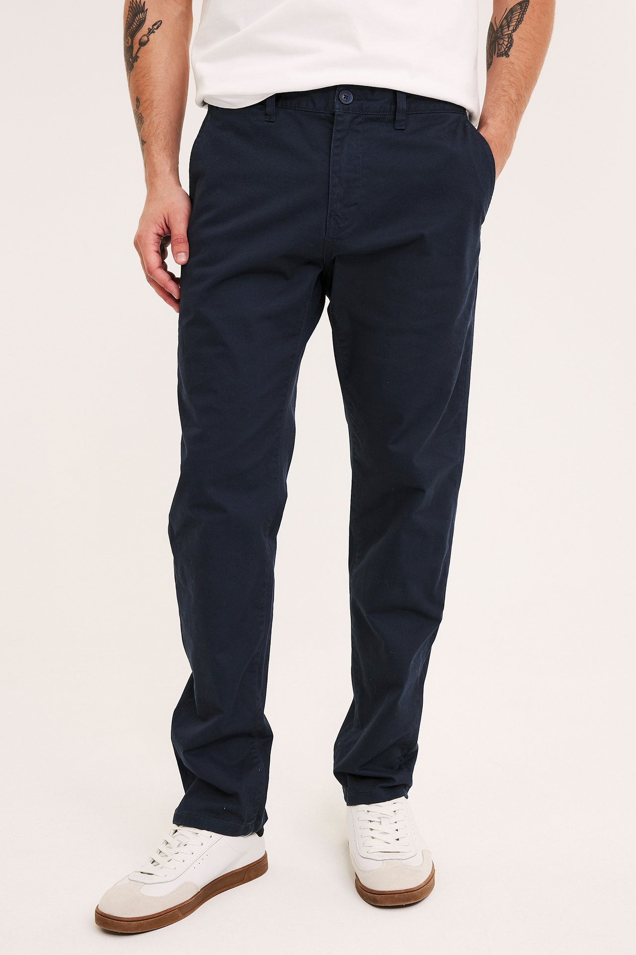 Frontbilde av en mann i mørkeblå regular fit chinos, en hvit t-skjorte og hvite joggesko.