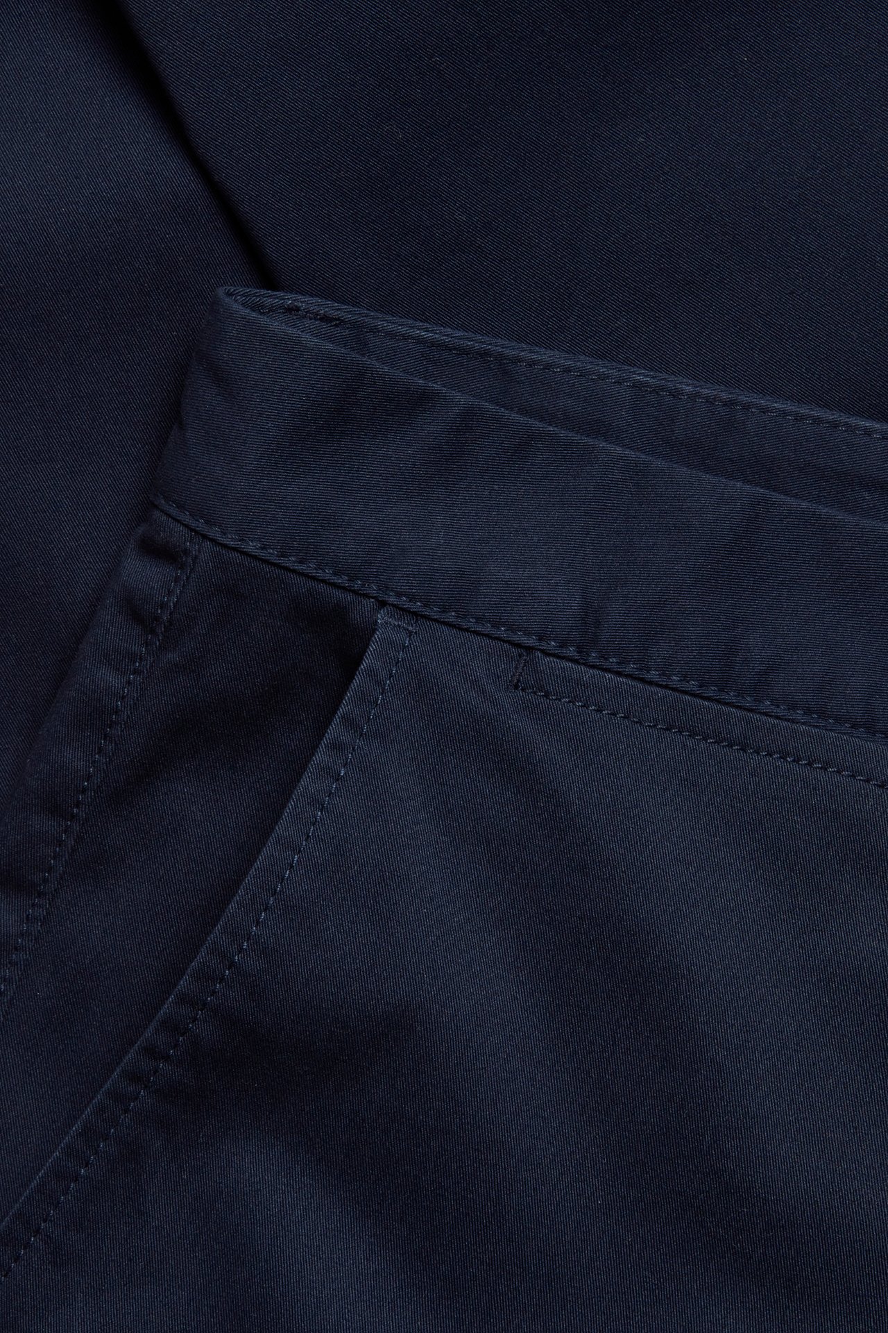 Zbliżenie na granatowe chinosy regular fit z bawełny z elastanem, pokazujące kieszeń i pas.