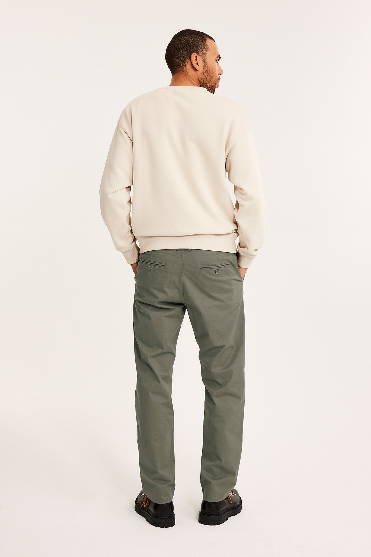 Bakifrån: man i gröna regular fit chinos, en beige sweatshirt och mörka skor.