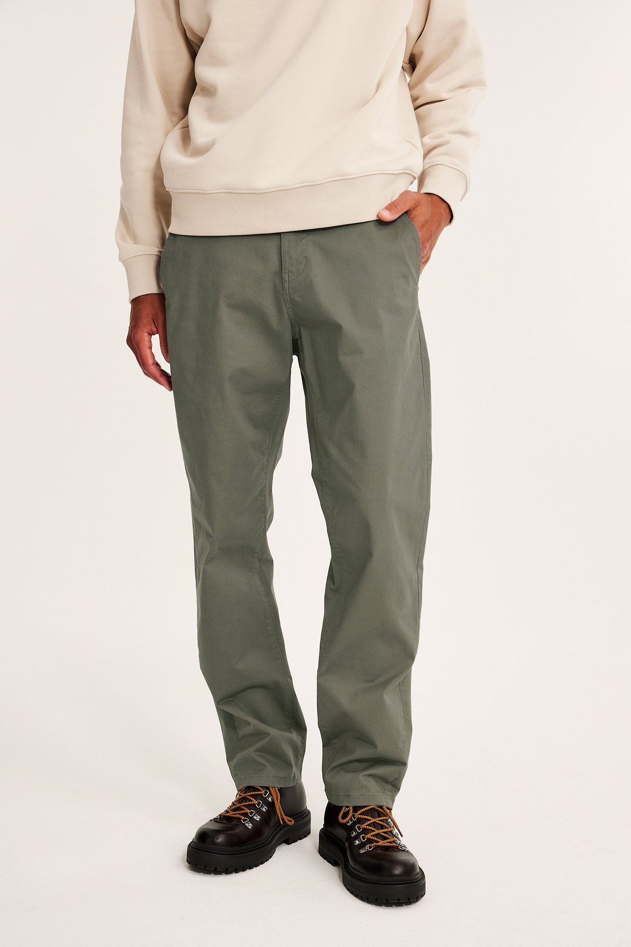 Edestä kuvattu mies yllään vihreät regular fit chinot, beige collegepaita ja tummanruskeat nauhakengät.