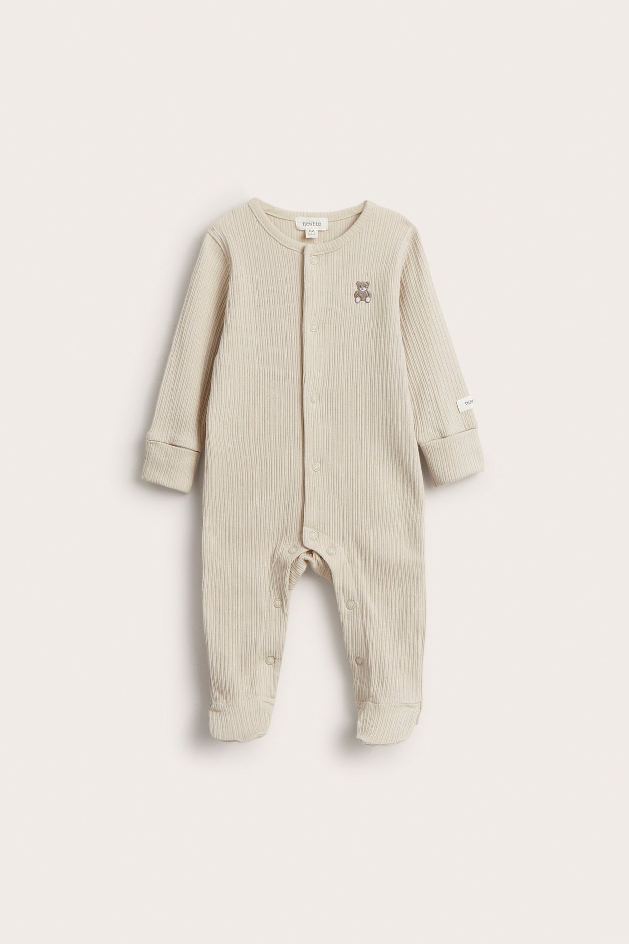 Etunäkymä: Beige ribattu vauvan pyjama neppareilla, jalkaterällinen malli ja nallekirjailu.