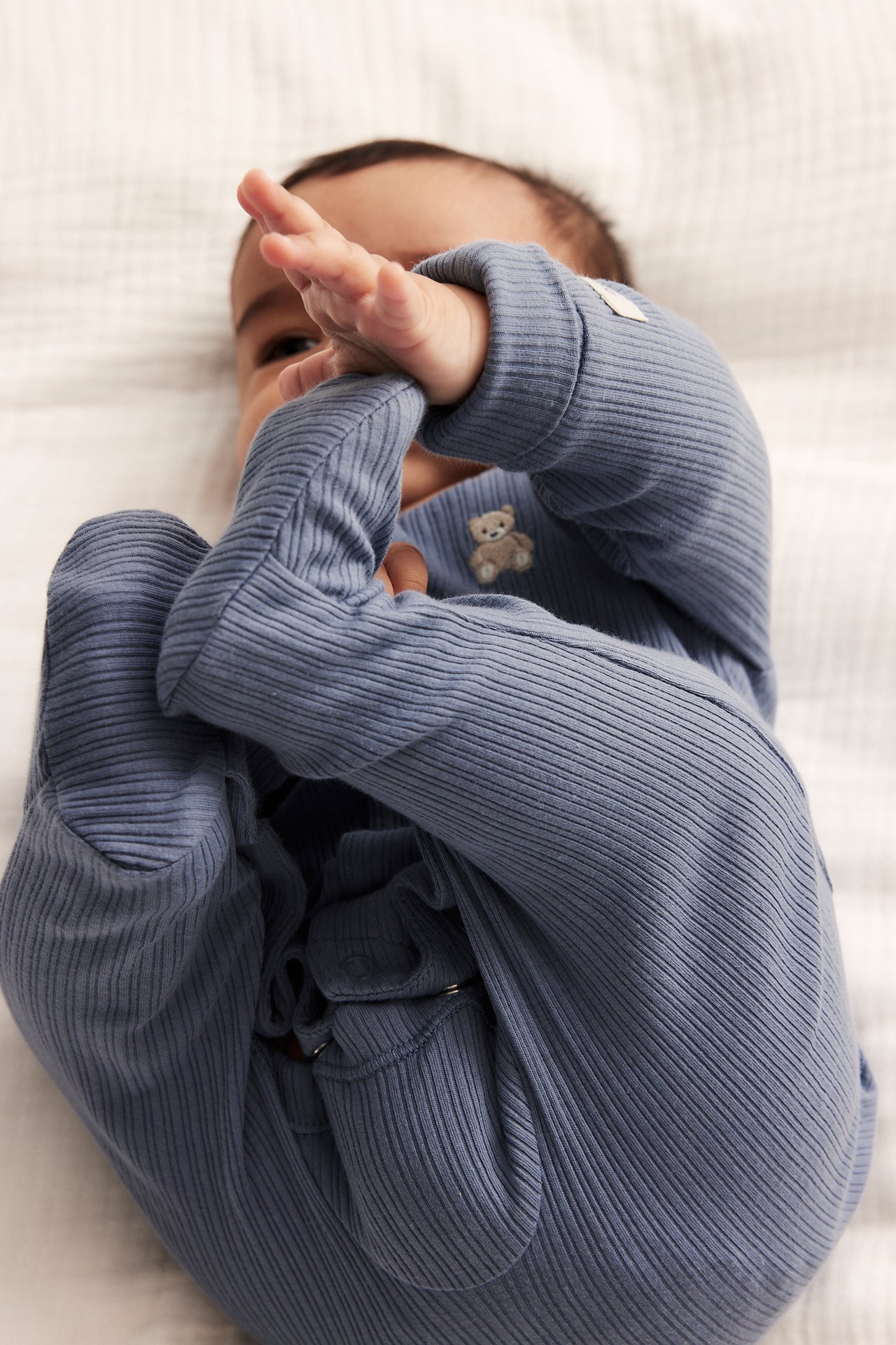 Lähikuva vauvasta sinisessä ribbipyjamassa, jossa nallekirjailu ja painonapit.