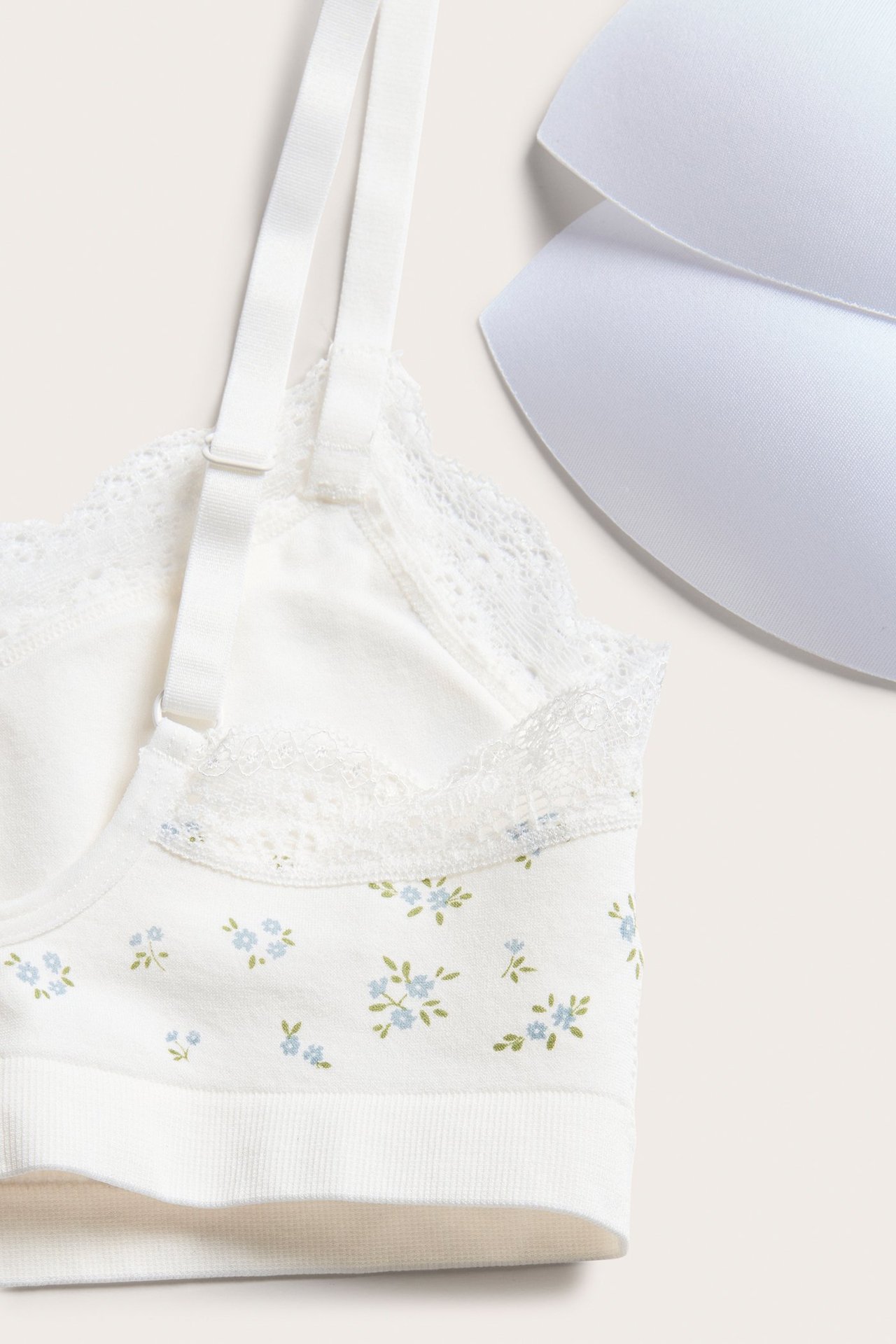 Zbliżenie białego bezszwowego topu biustonosza z niebieskim kwiatowym wzorem, koronką, regulowanymi ramiączkami i dwoma wkładkami.