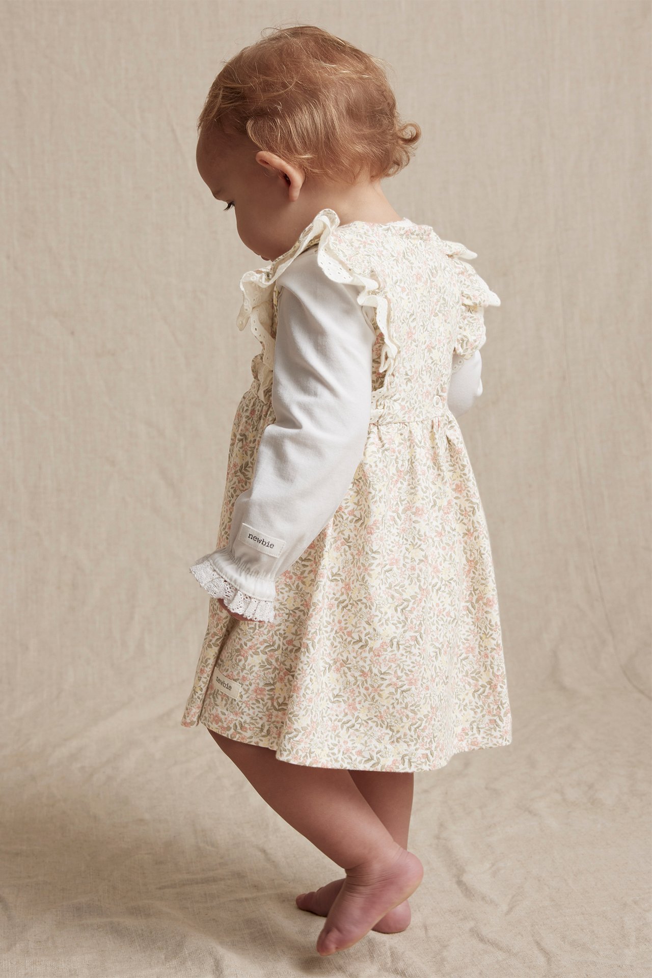Off-white blomstret jerseystrikket kjole med blonderynker, båret av en baby over en hvit langermet topp.