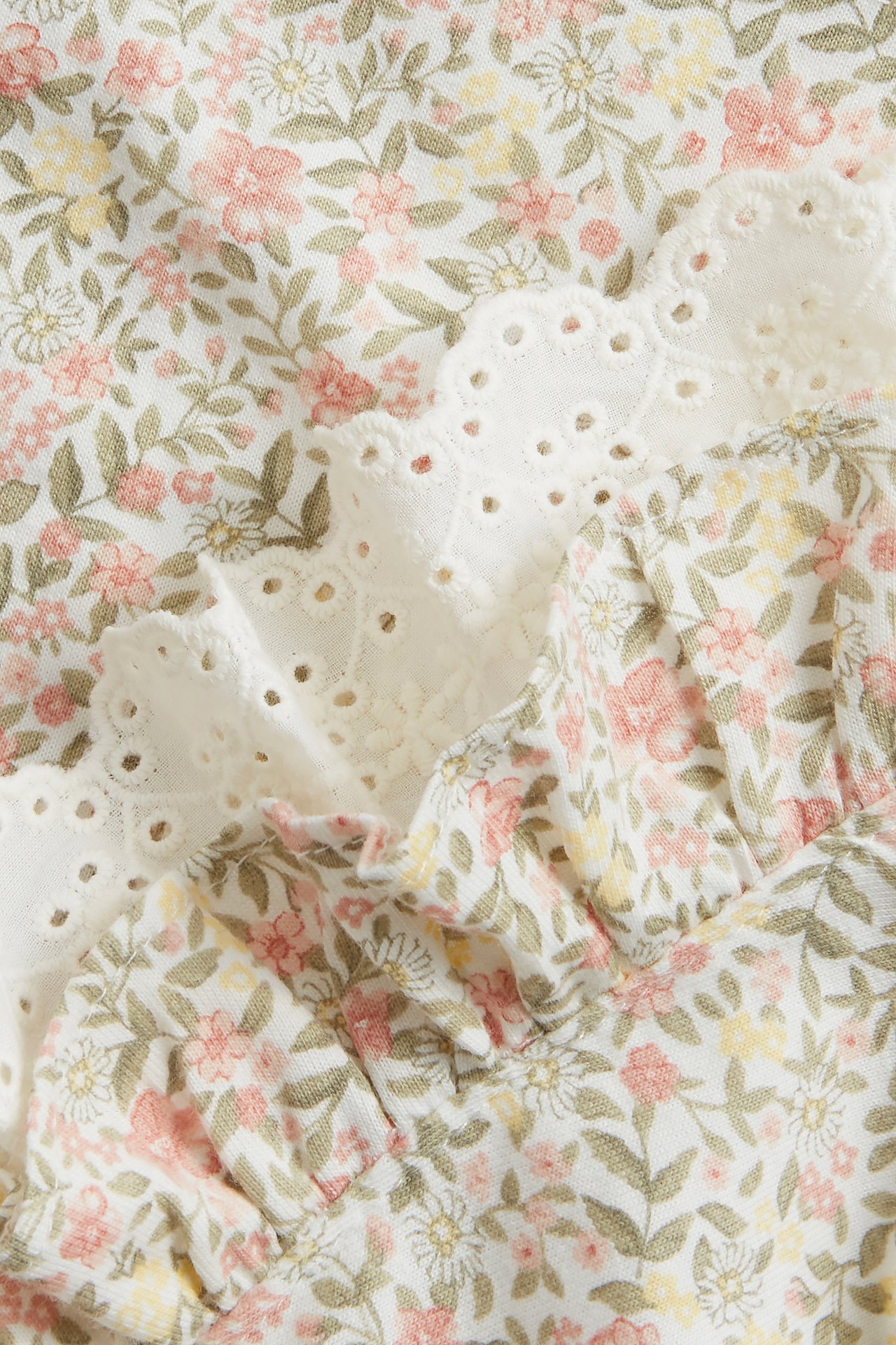 Nærbilde av en offwhite bomullskjole med blomstermønster, volang og hvit blondekant.