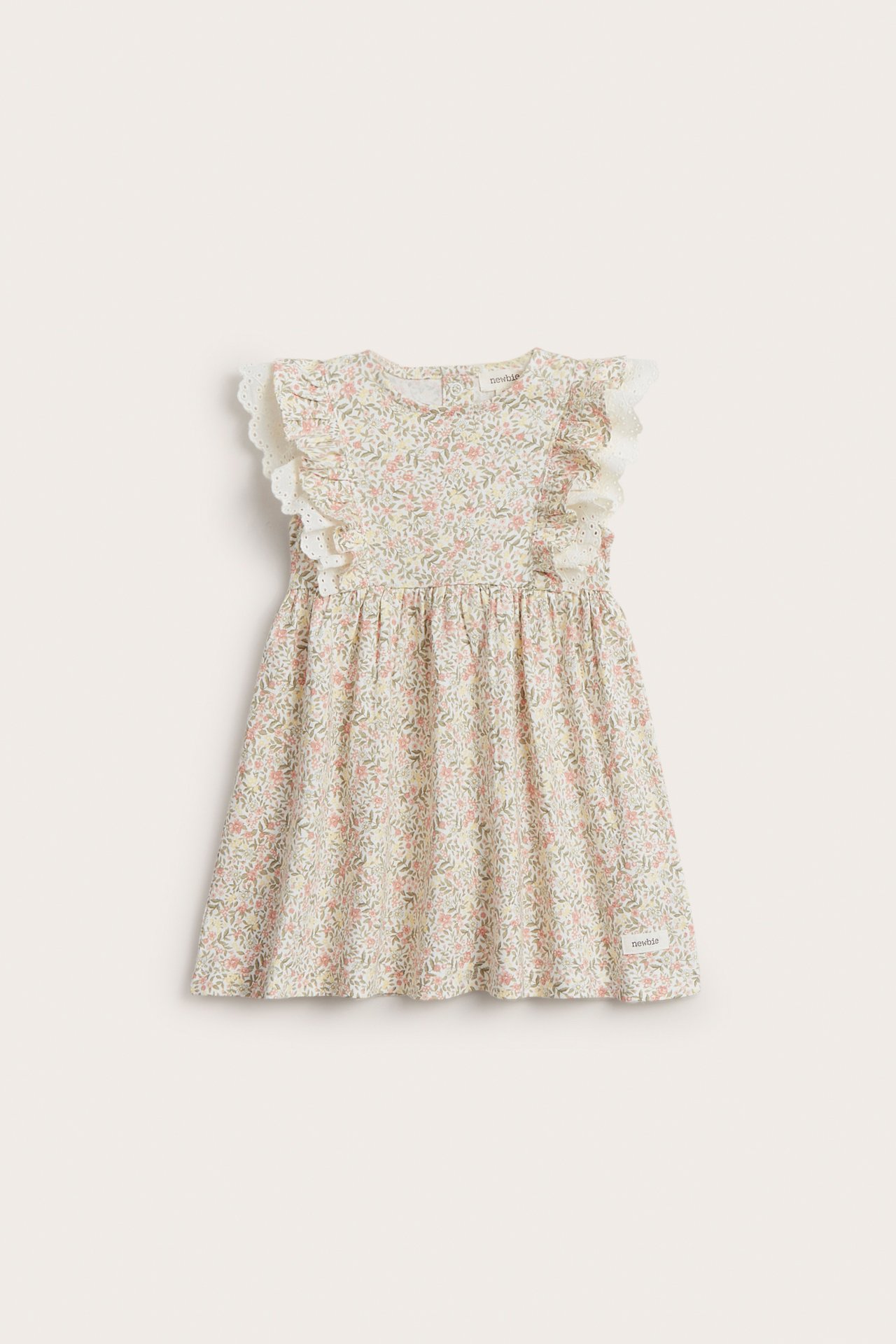 Frontvisning av en offwhite ermeløs babykjole i bomull med småblomstret mønster og volang med blondekant.