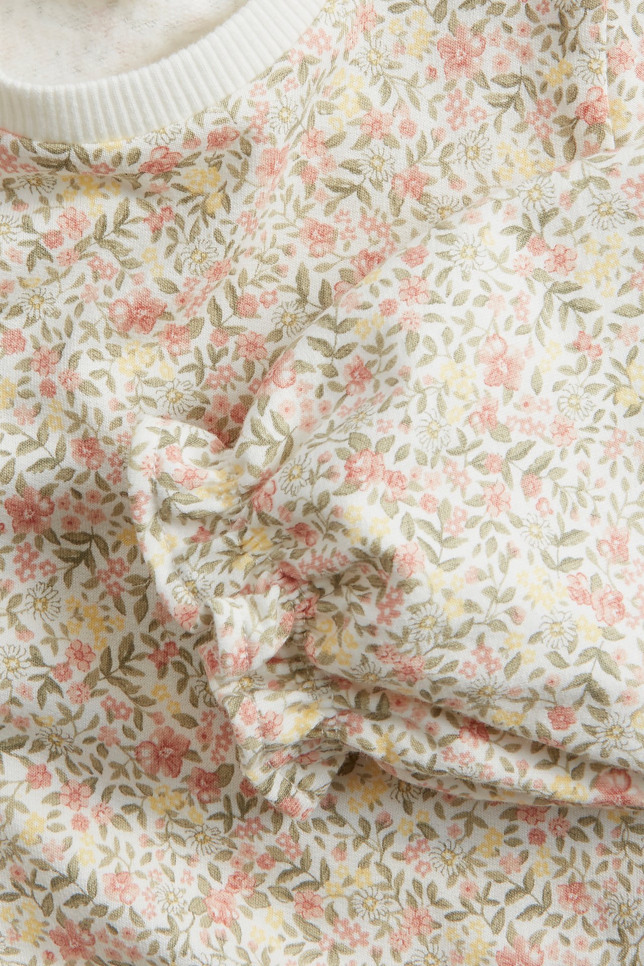 Nærbilde av en offwhite bomullssweatshirt med blomstermønster, ribbet hals og volangerm.