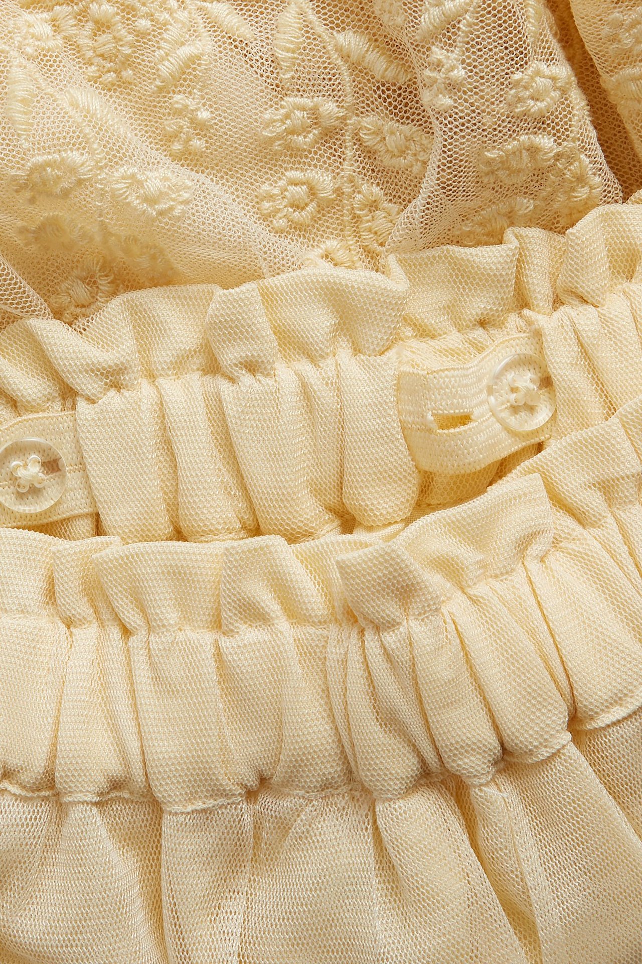 Zbliżenie żółtej spódnicy z siateczki z haftowanymi wzorami kwiatowymi i falbankowym elastycznym pasem z guzikami.