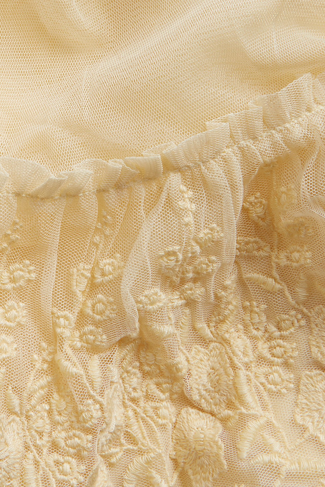 Nærbilde av et gult meshskjørt med broderte blomstermønstre og en volangkant.