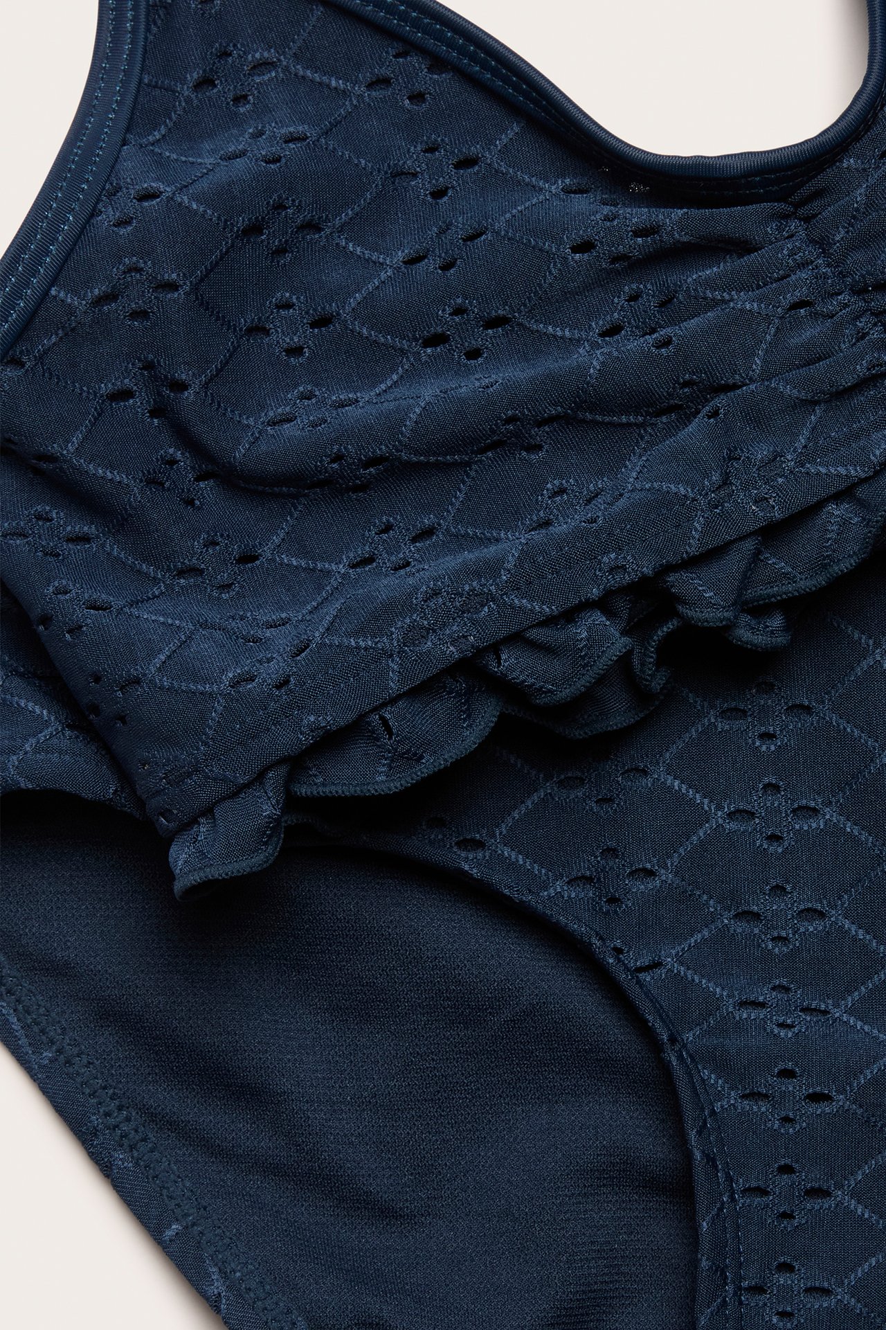 Zbliżenie na ciemnoniebieskie dziecięce bikini z haftem angielskim i falbankami na górze.