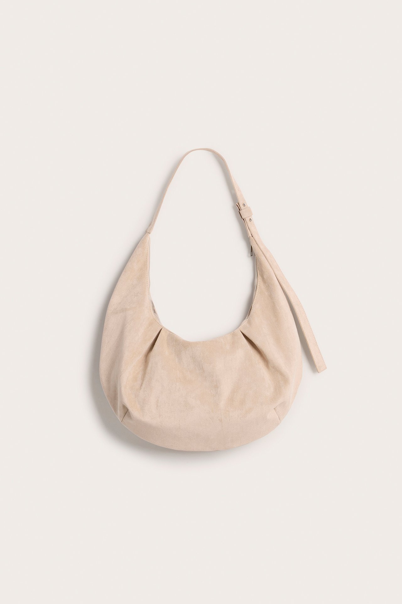 Forfra, beige halvmåneformet skulderveske i imitert semsket skinn med justerbar stropp.