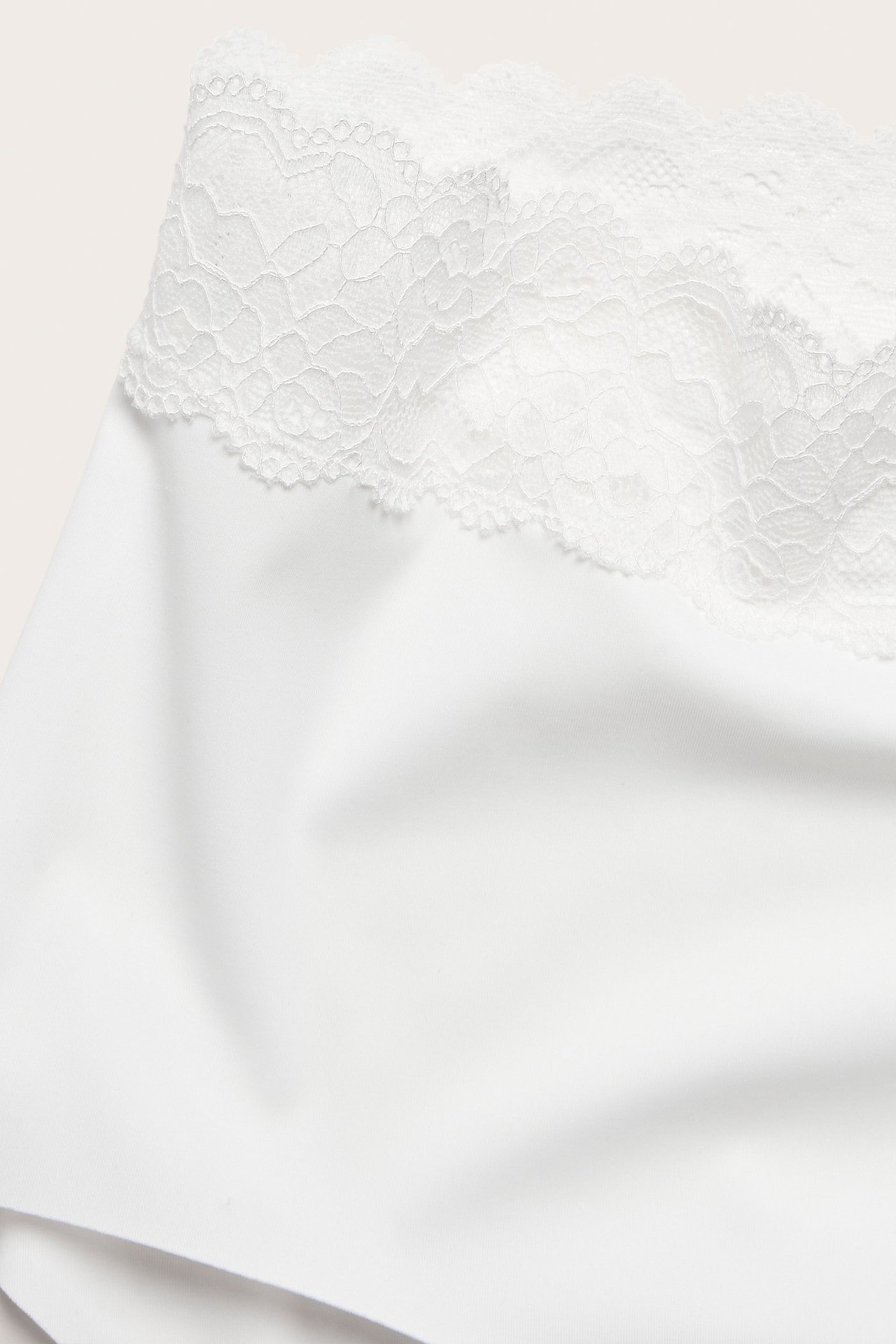 Zbliżenie na białe, gładkie figi typu hipster z podwyższonym stanem i miękką koronkową lamówką.