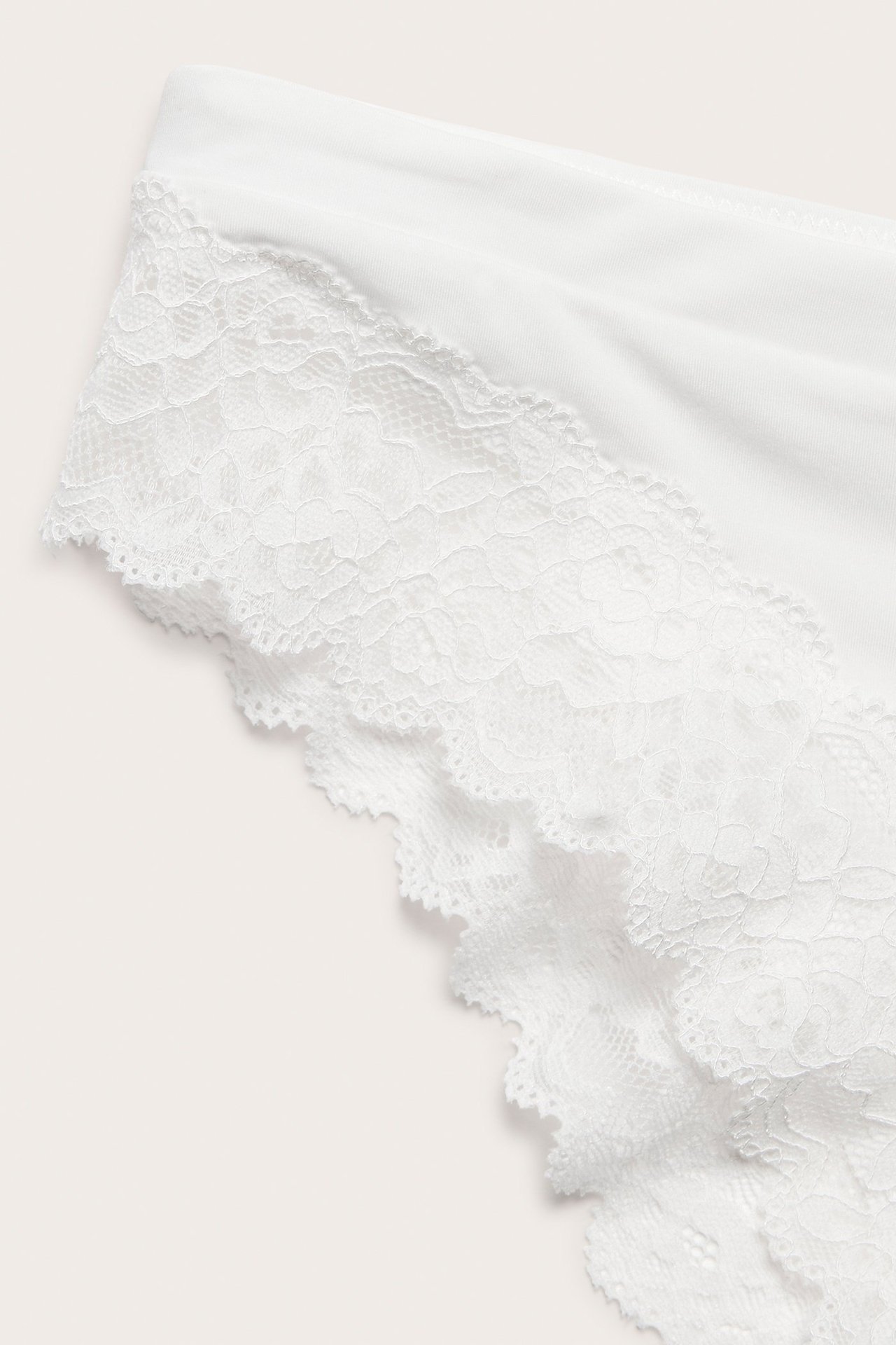 Zbliżenie na białe majtki damskie typu brazilian z mikrofibry z koronkowym wykończeniem.