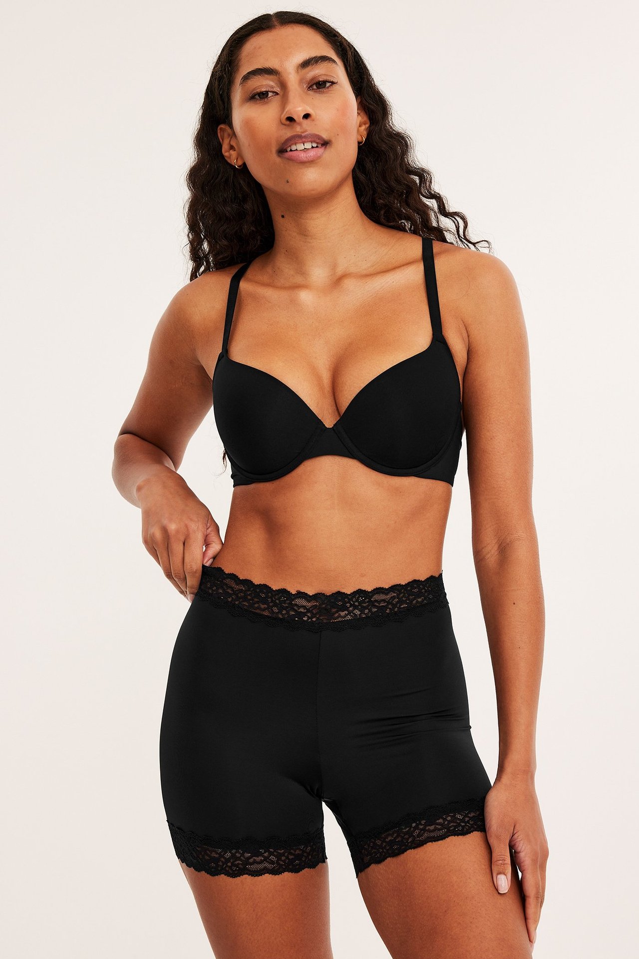 Frontbilde av en kvinne i svarte, tettsittende shorts med blondekant og en svart push-up BH.