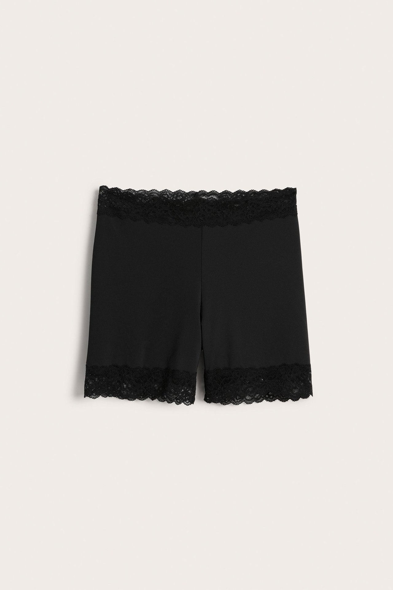 Forfra: svarte ensfargede dameshorts med blondekant i midjen og benåpningene.