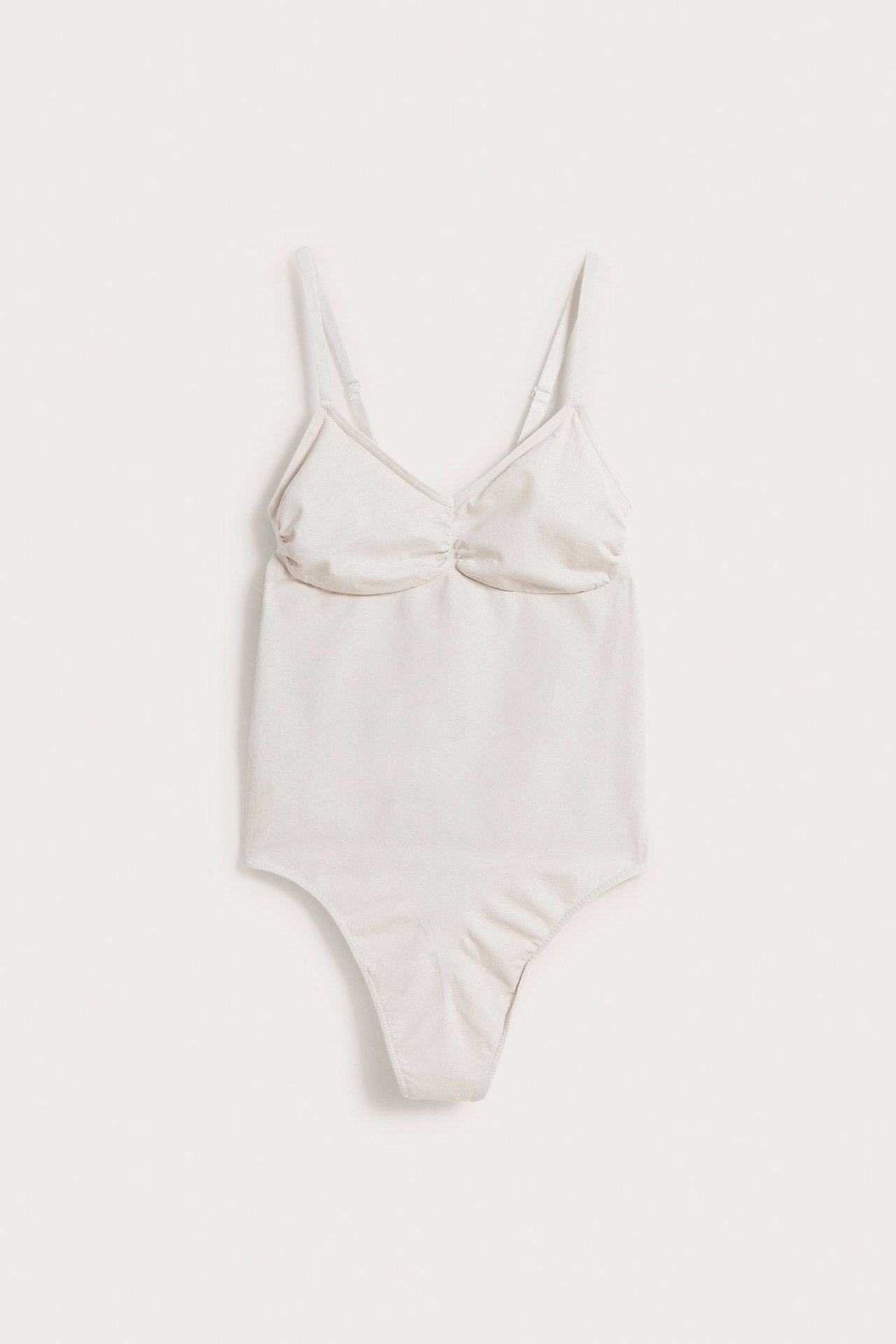 Forfra, beige sømløs shapingbody med justerbare stropper og stringtruser.