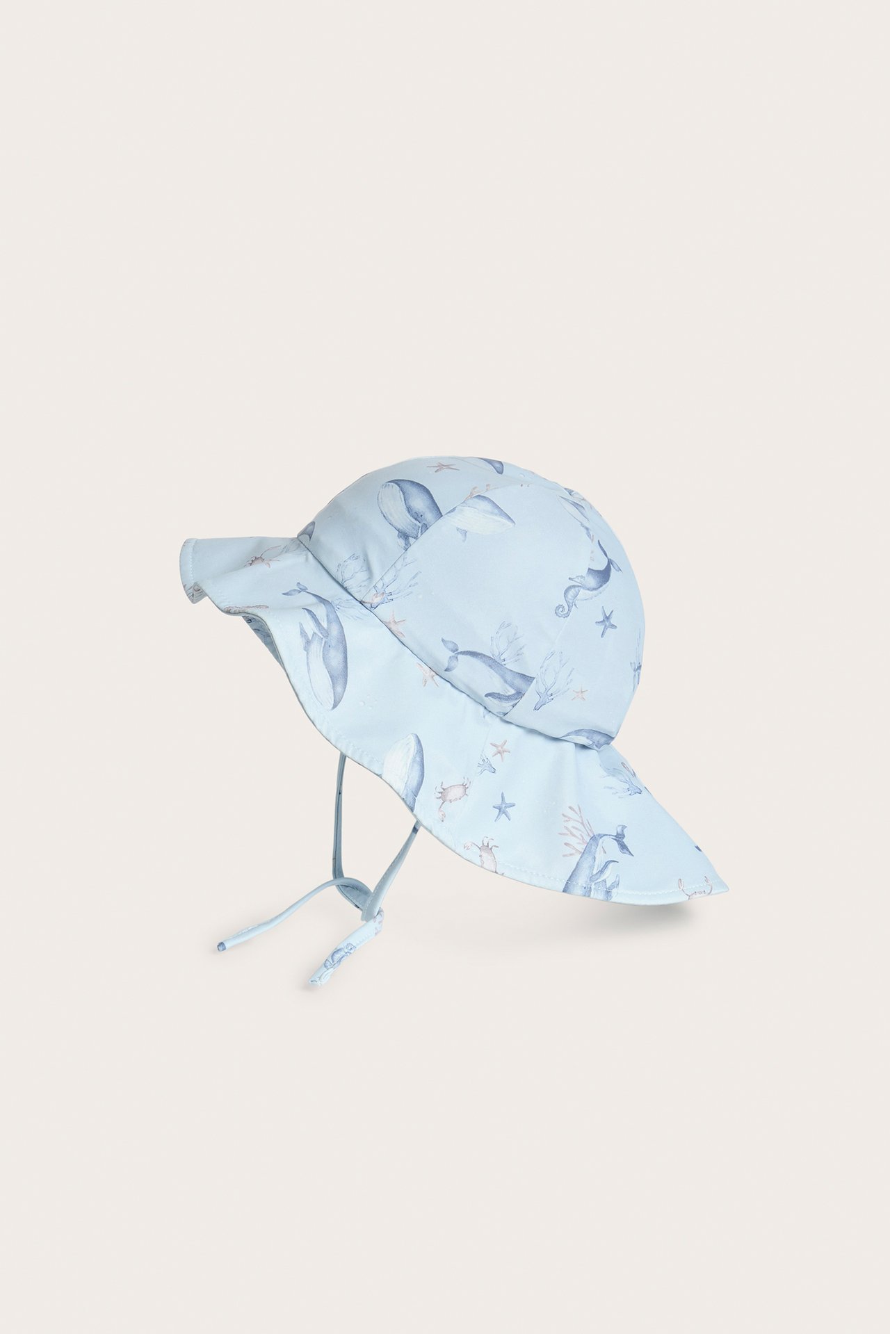 Sidevisning av en lyseblå baby solhatt med hval- og sjødyrmønster og knytebånd.