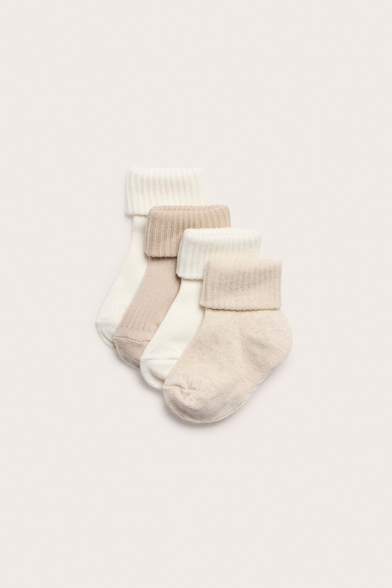 Ovanifrån: 4-pack ribbade babysockor i ljusbeige och benvitt med vikta muddar.