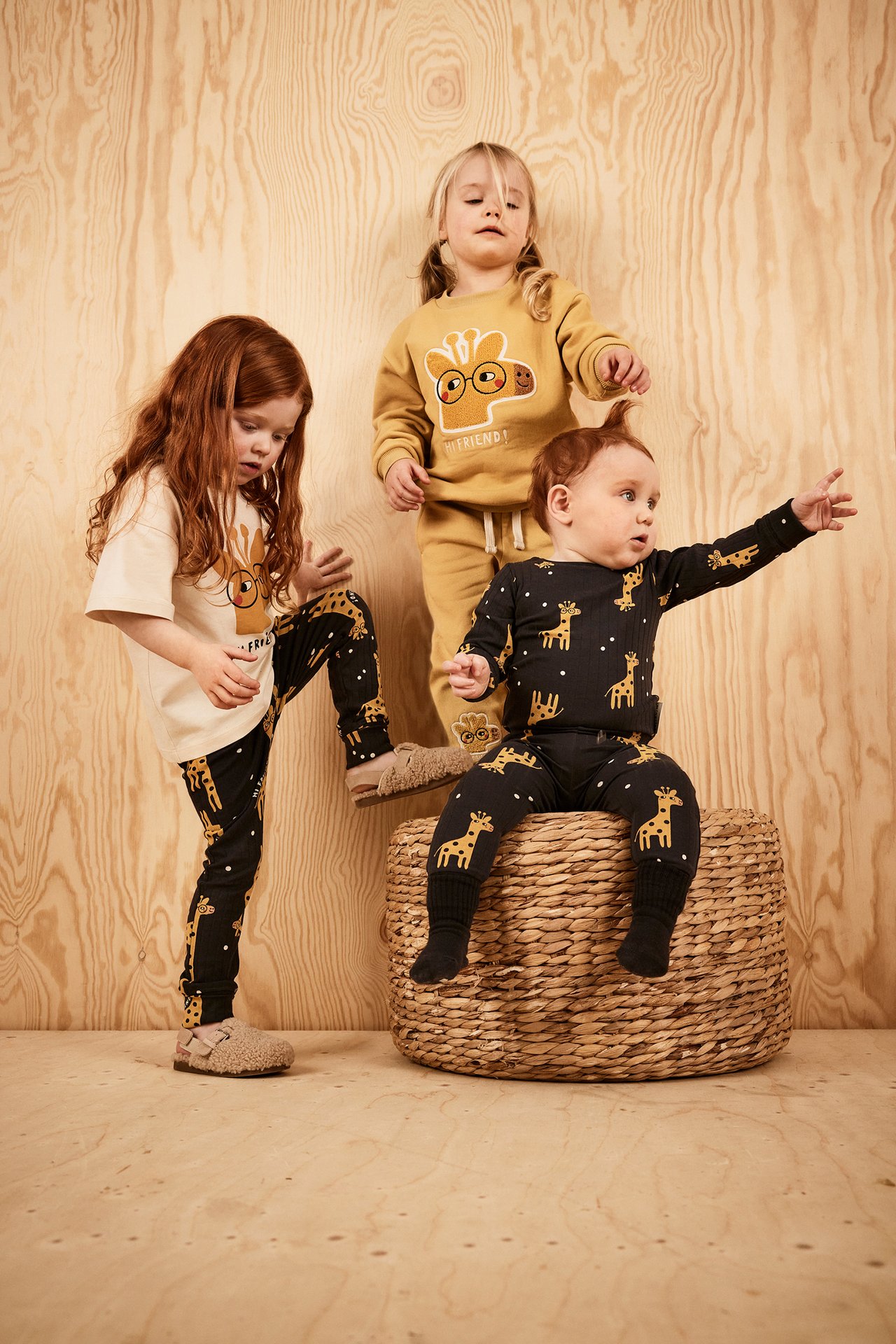 Frontvisning: Barn i beige bomulls-t-skjorte med sjirafftrykk, svarte leggings. Andre barn har sjiraffmønstrede sett.