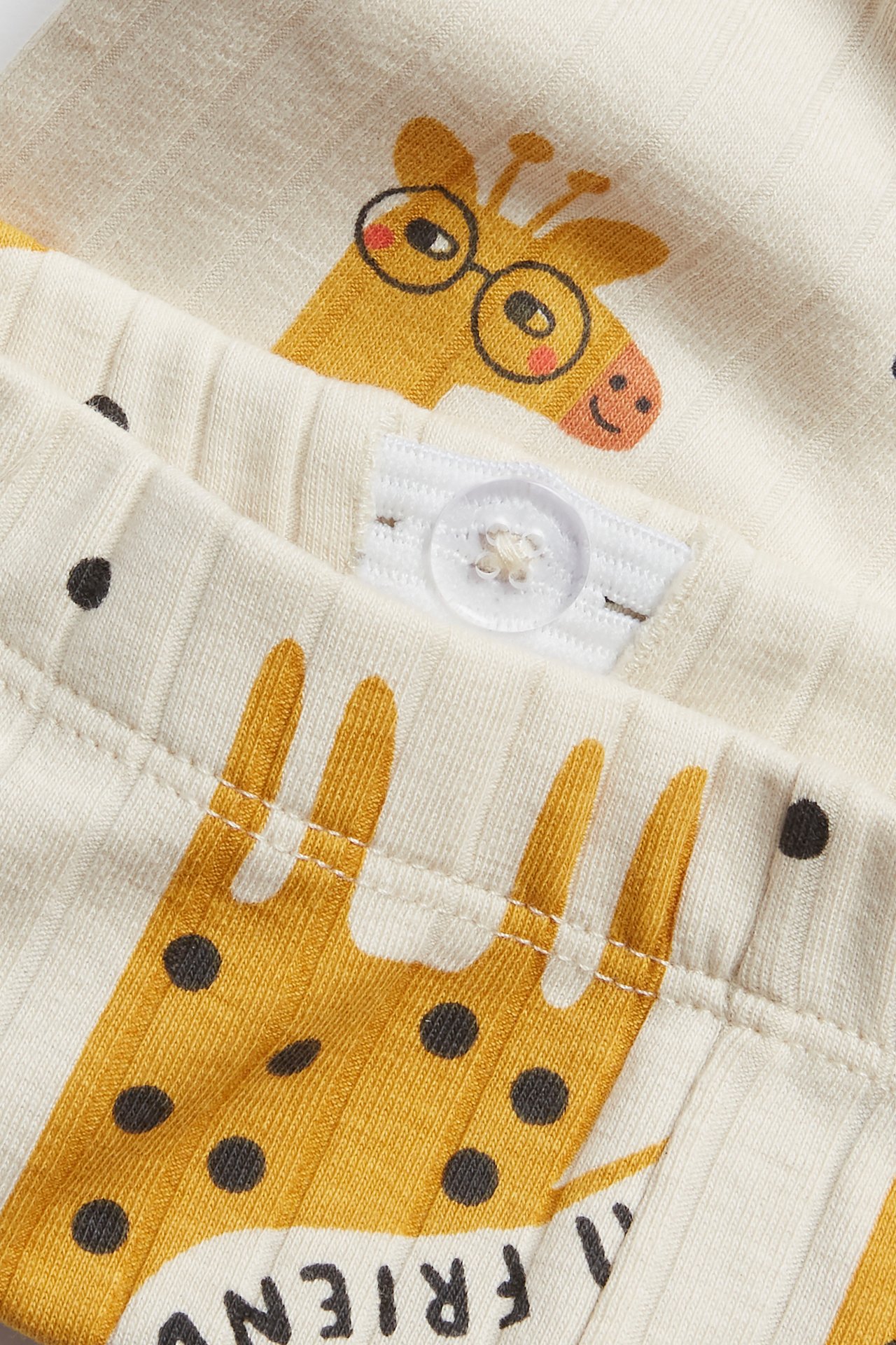 Närbild av beiga ribbade barnleggings med giraffmönster och justerbar midjeknapp.