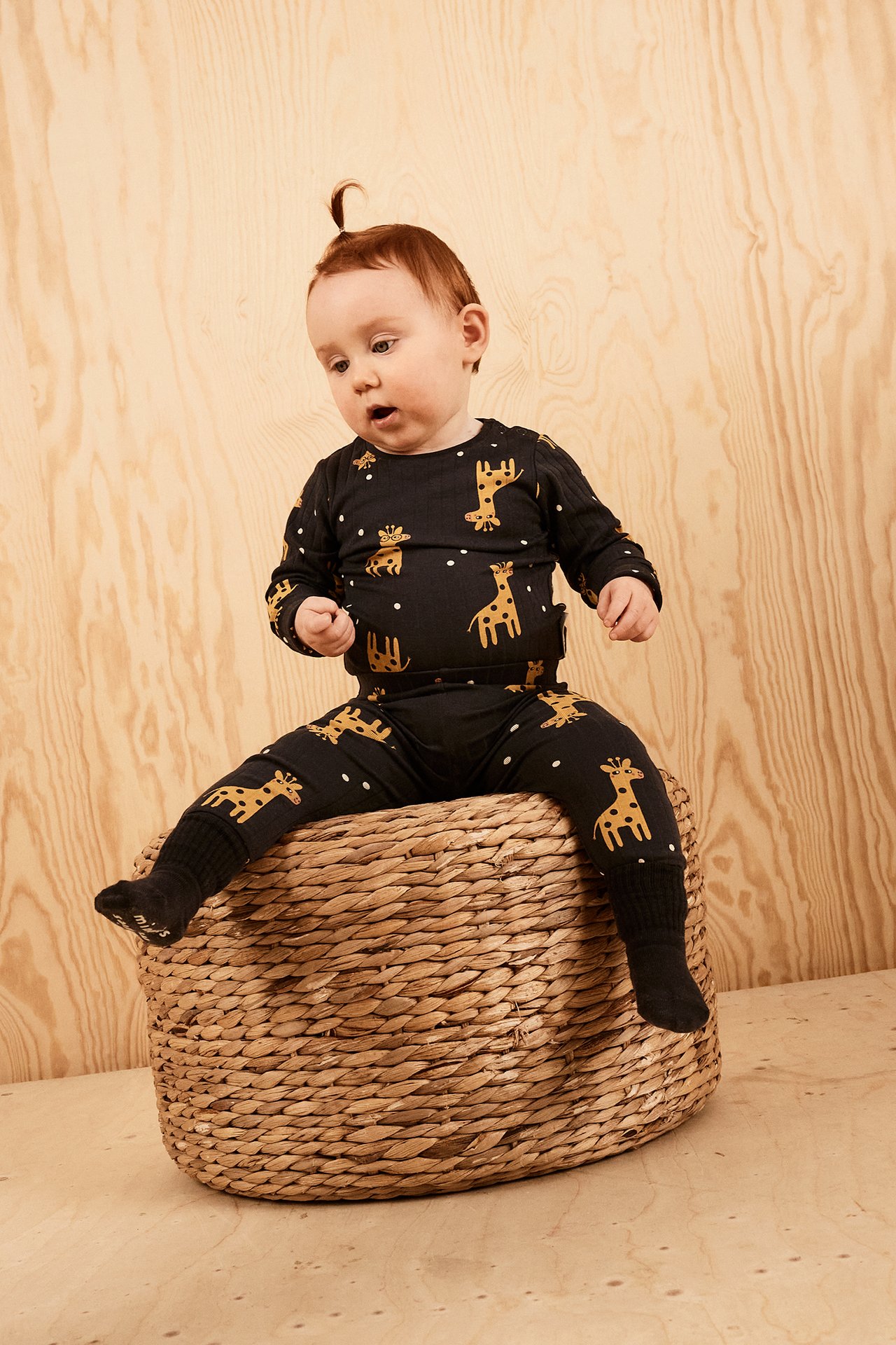 Frontvy av en baby i svart ribbad body med guldfärgat girafftryck och vita prickar, samt svarta strumpor.