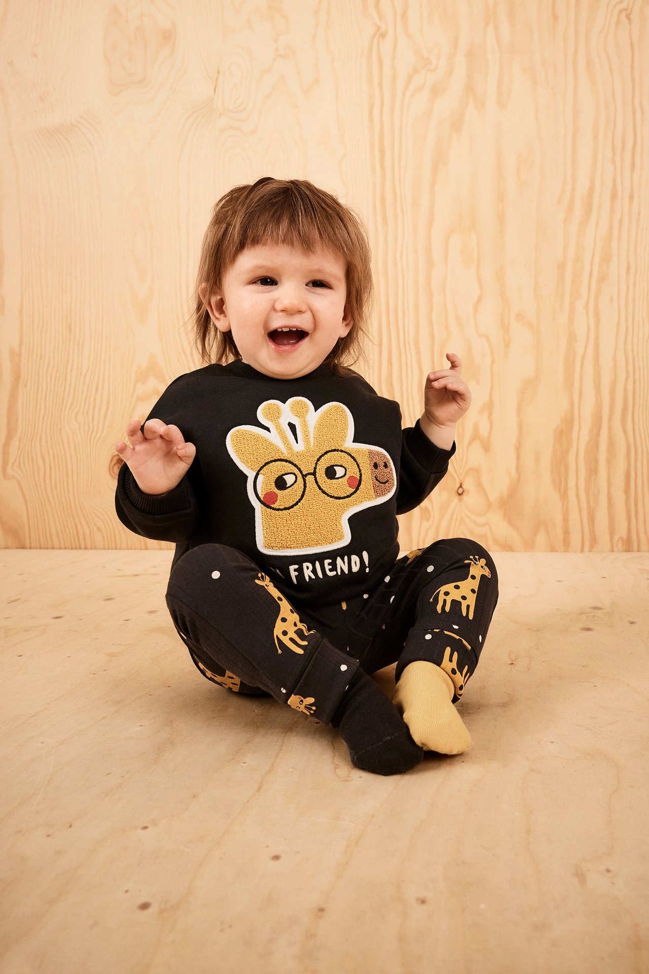 Framifrån, baby i svarta mönstrade leggings med girafftryck och en svart tröja med giraffapplikation.