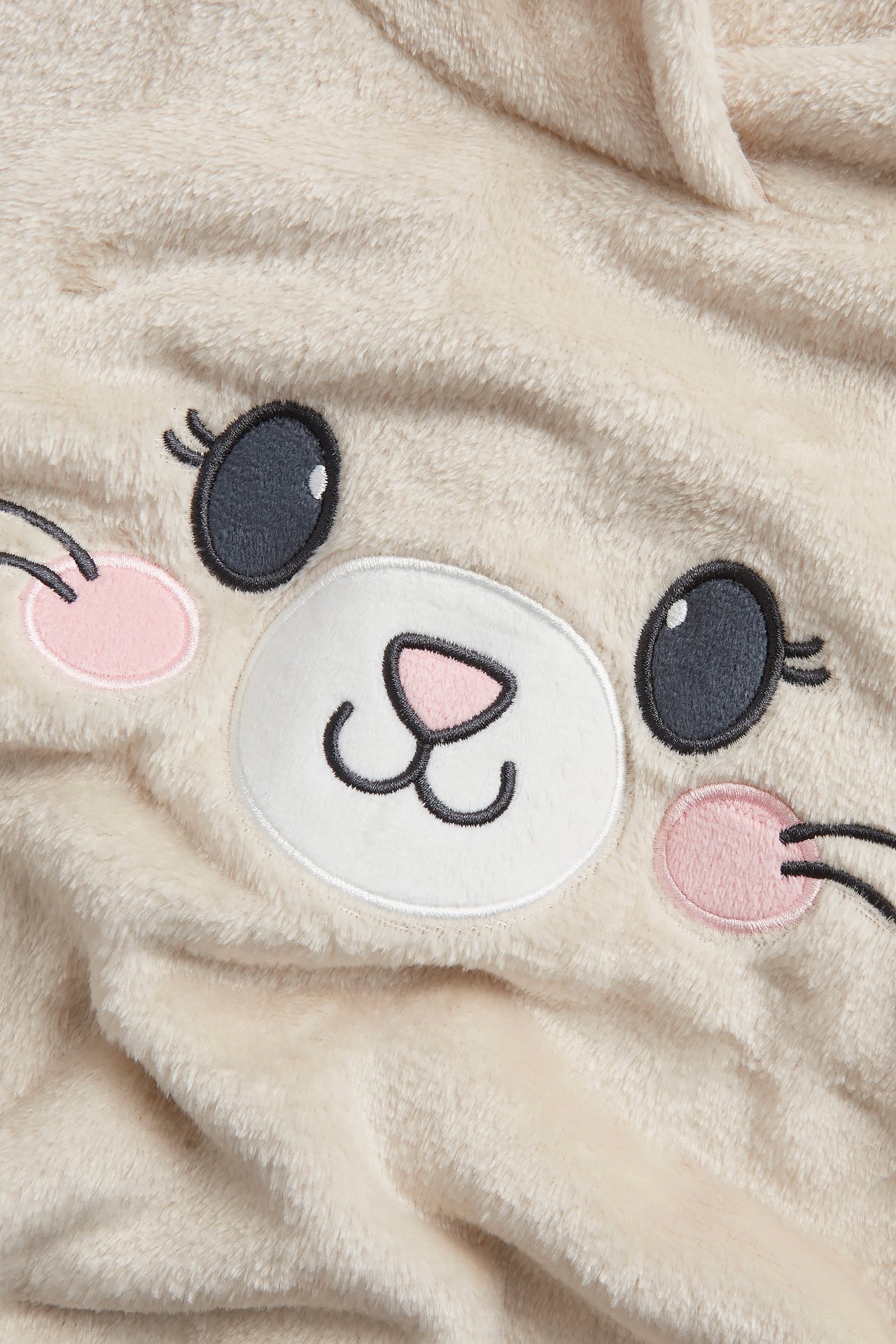Nærbilde av en beige lodden fleecehettegenser med brodert katteansikt og ører.