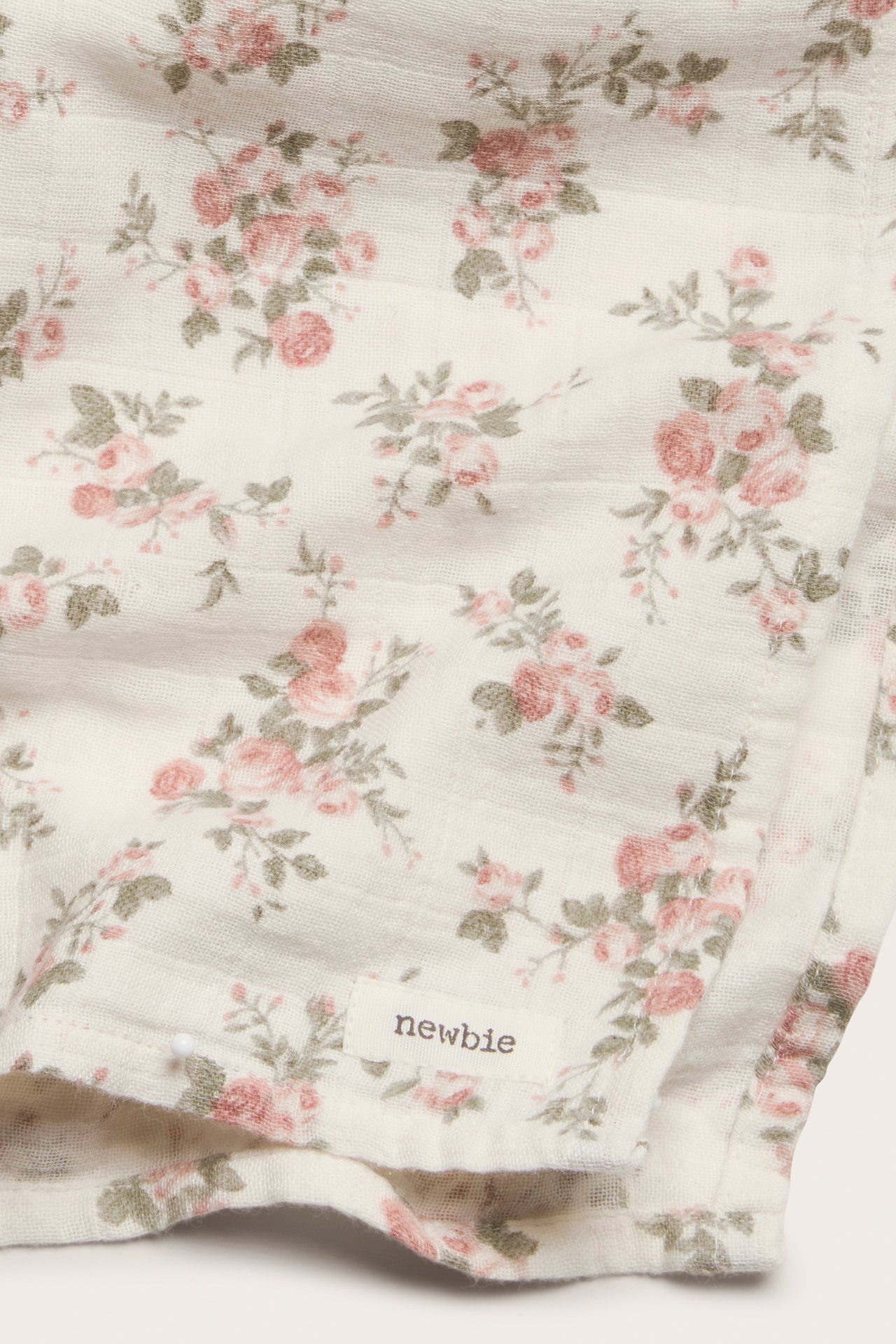 Närbild av en offwhite bomullsmuslinfilt med rosa blommönster och en 'newbie'-etikett.