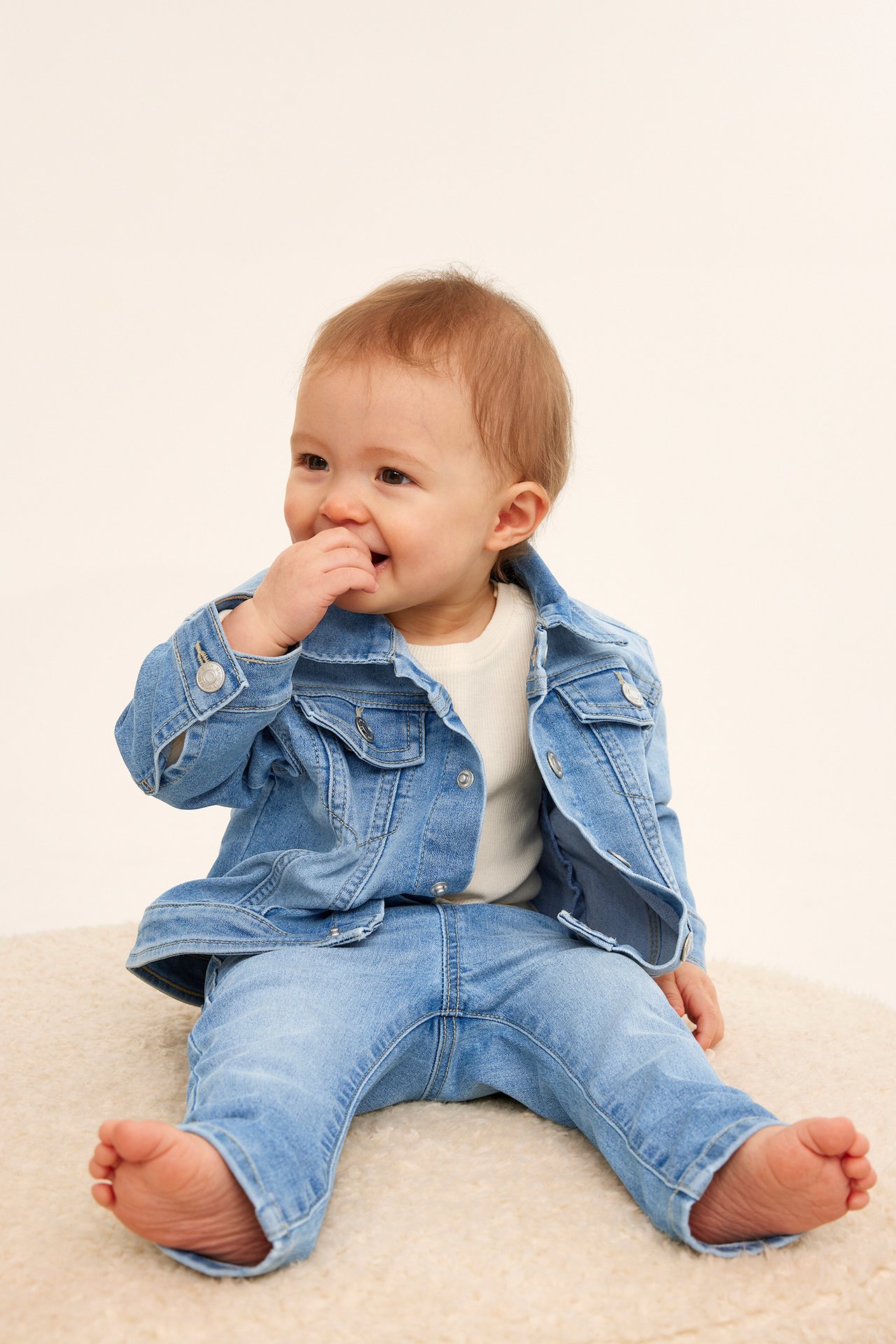 Framifrån av en baby i ljusblå denimjeggings, matchande denimjacka och en krämfärgad topp.