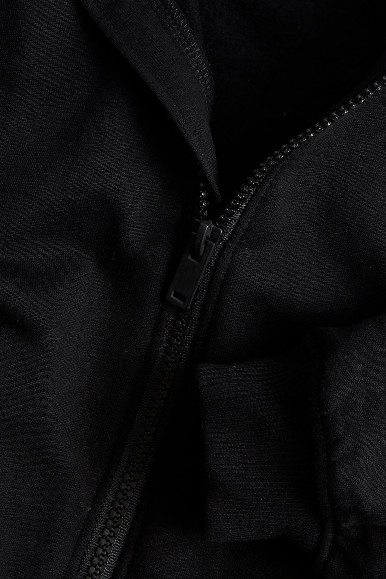 Zbliżenie czarnego bawełnianego kardiganu z zamkiem błyskawicznym i prążkowanym mankietem.
