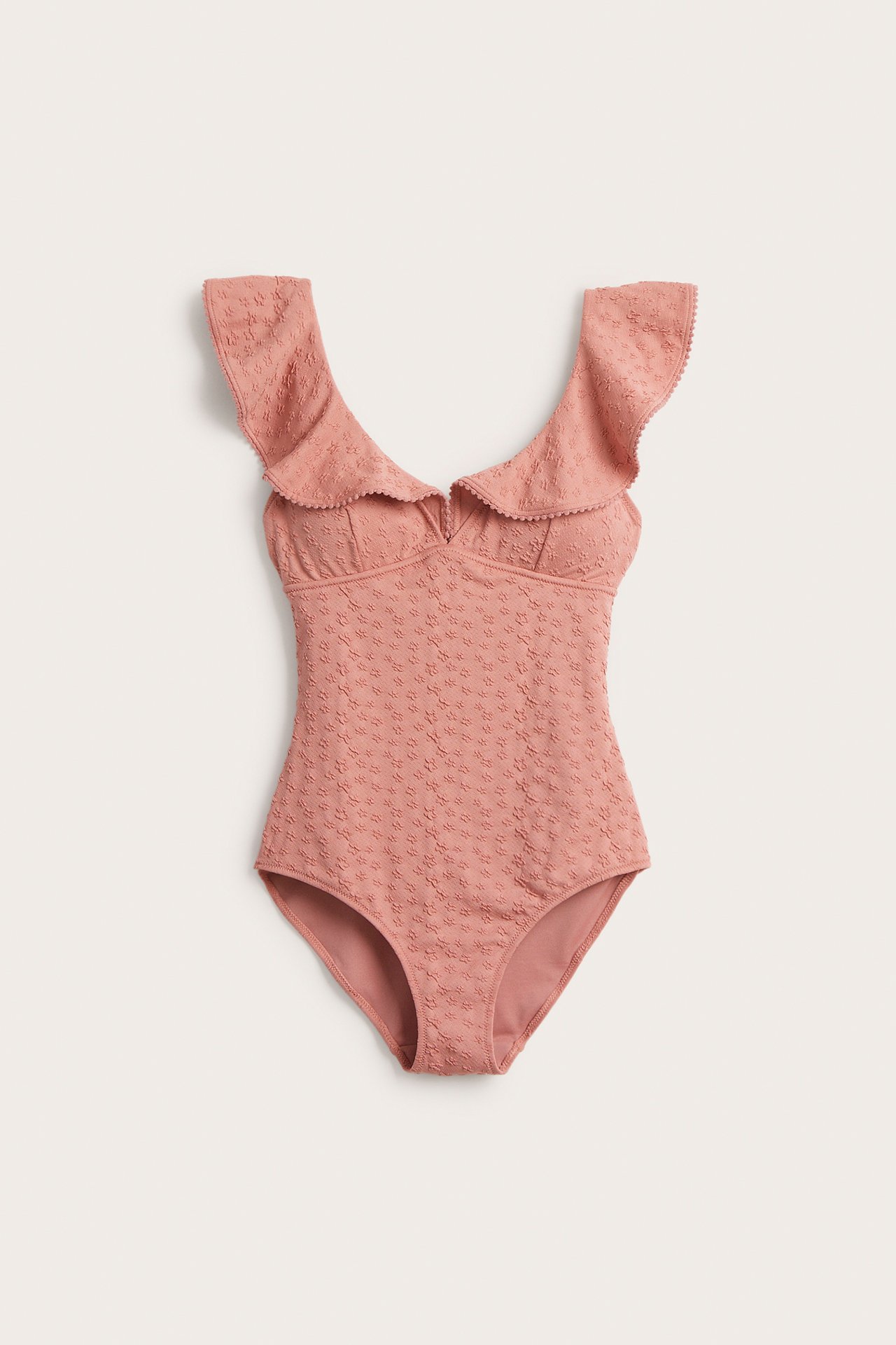 Frontvisning av en rosa damebadedrakt med jacquardblomster, store volanger og pom-pom-kant.