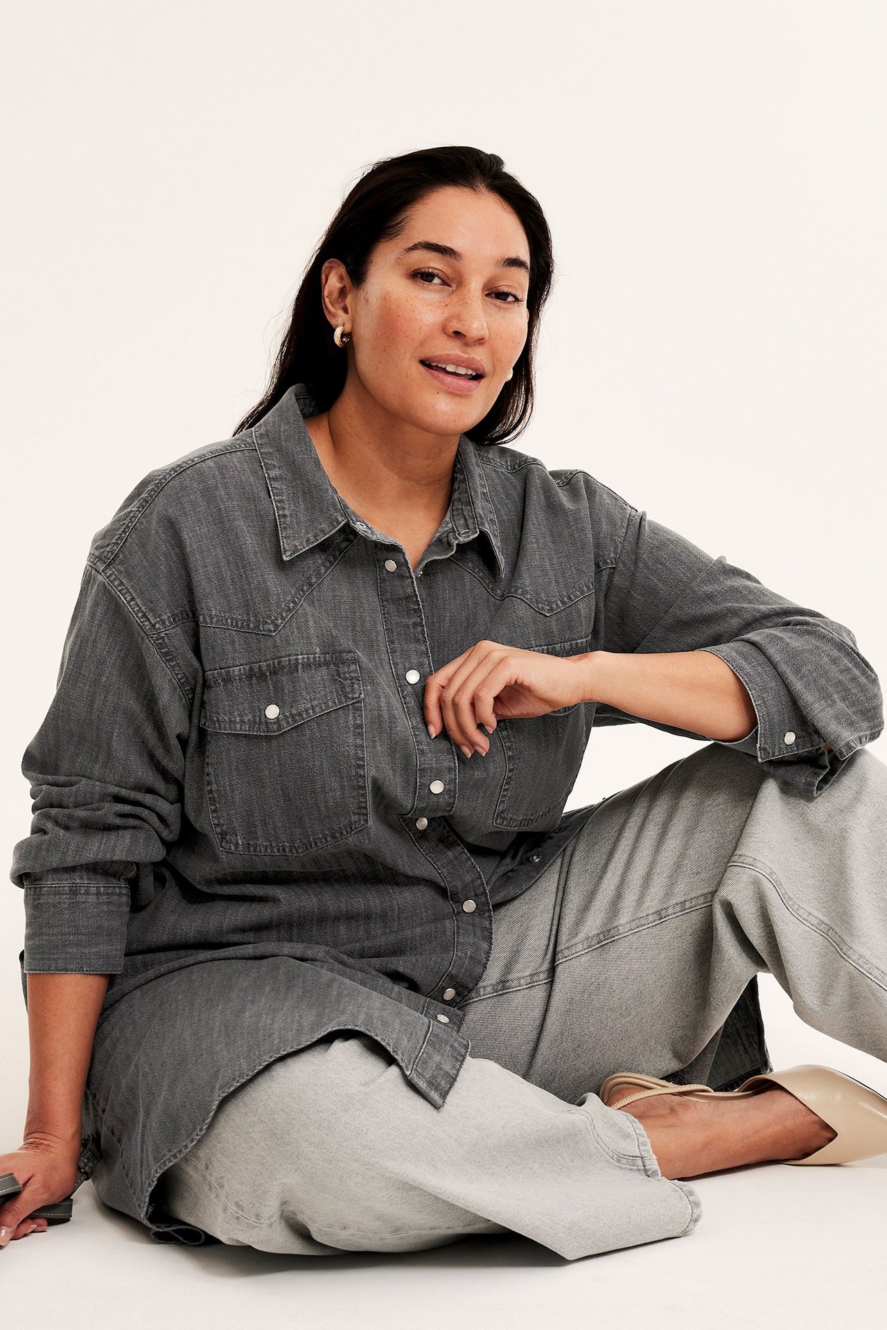 Edestä: nainen harmaassa farkkupaitamekossa, vaaleanharmaissa leveälahkeisissa farkuissa ja beigenvärisissä kengissä.