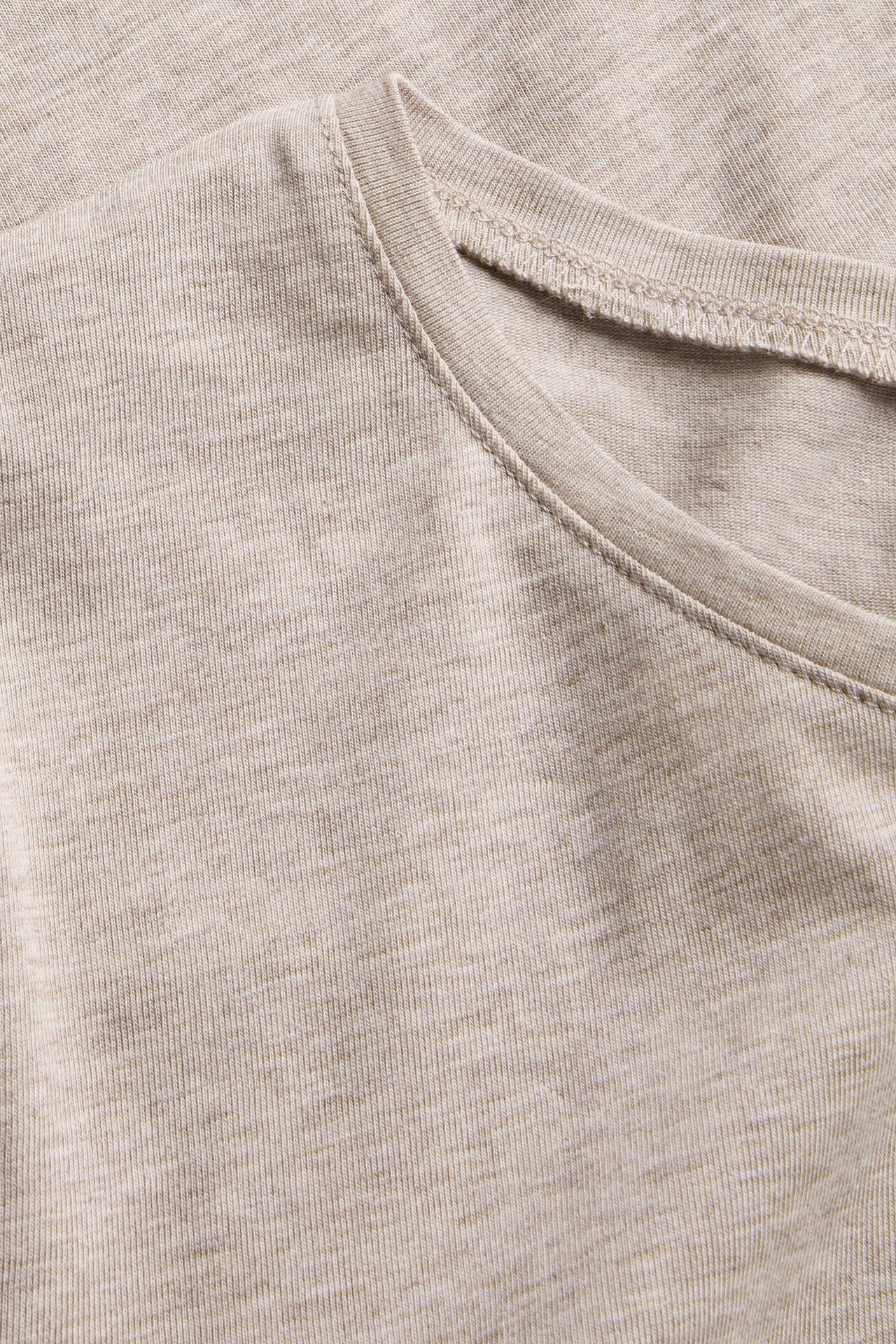 Zbliżenie beżowego melanżowego, krótkiego topu z okrągłym dekoltem.