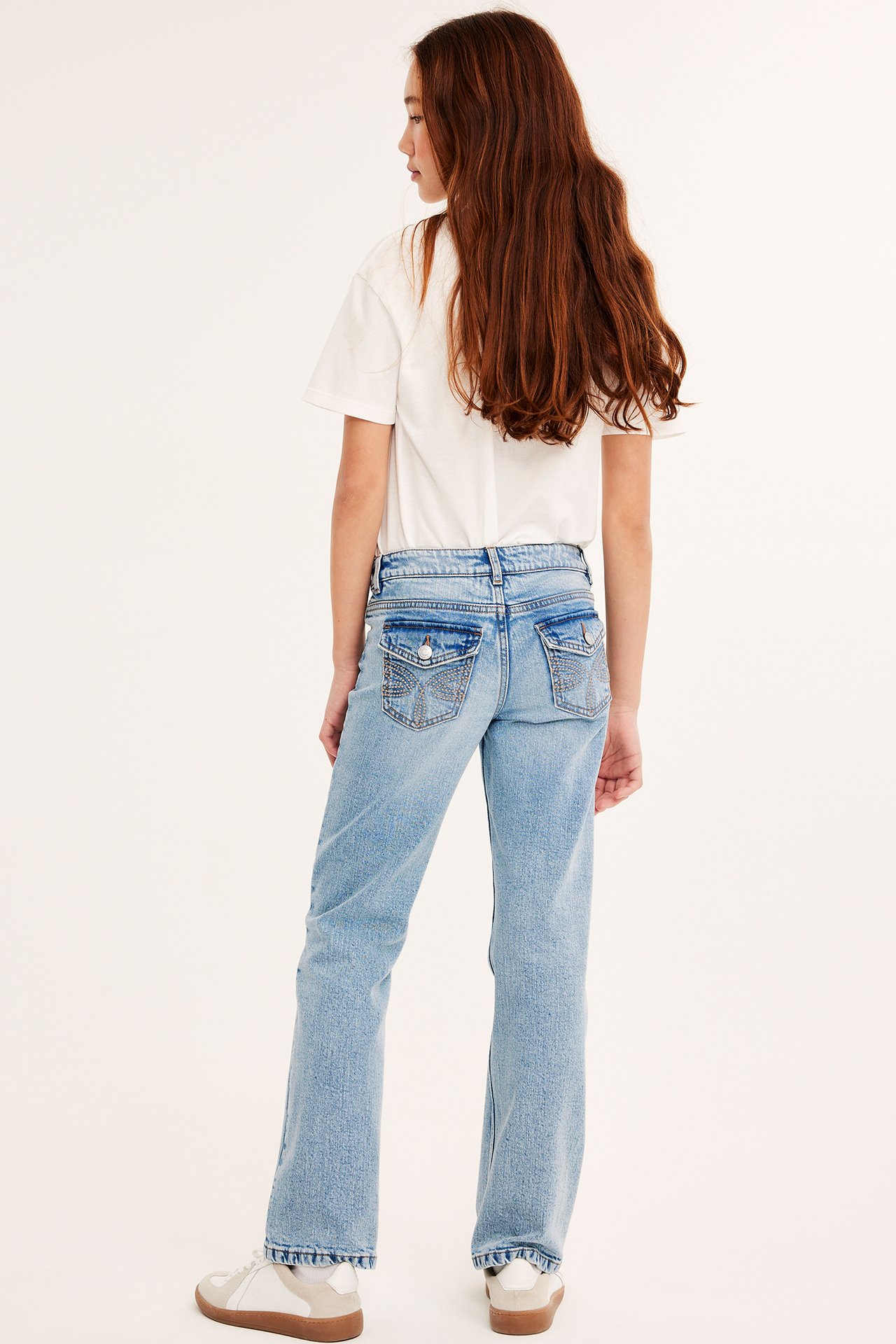 Bakifrån: Barn bär ljusa bootcut-jeans med låg midja, dekorativa bakfickor, vit t-shirt och sneakers.