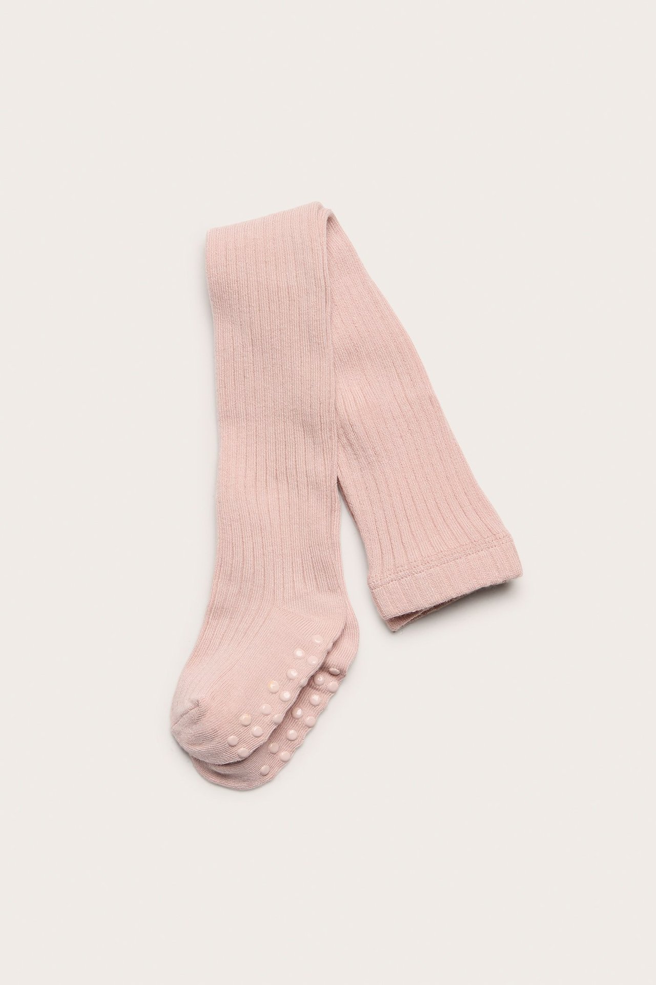 Ovanifrån vy av vikta ljusrosa ribbade babystrumpbyxor med antislip-prickar på sulorna.