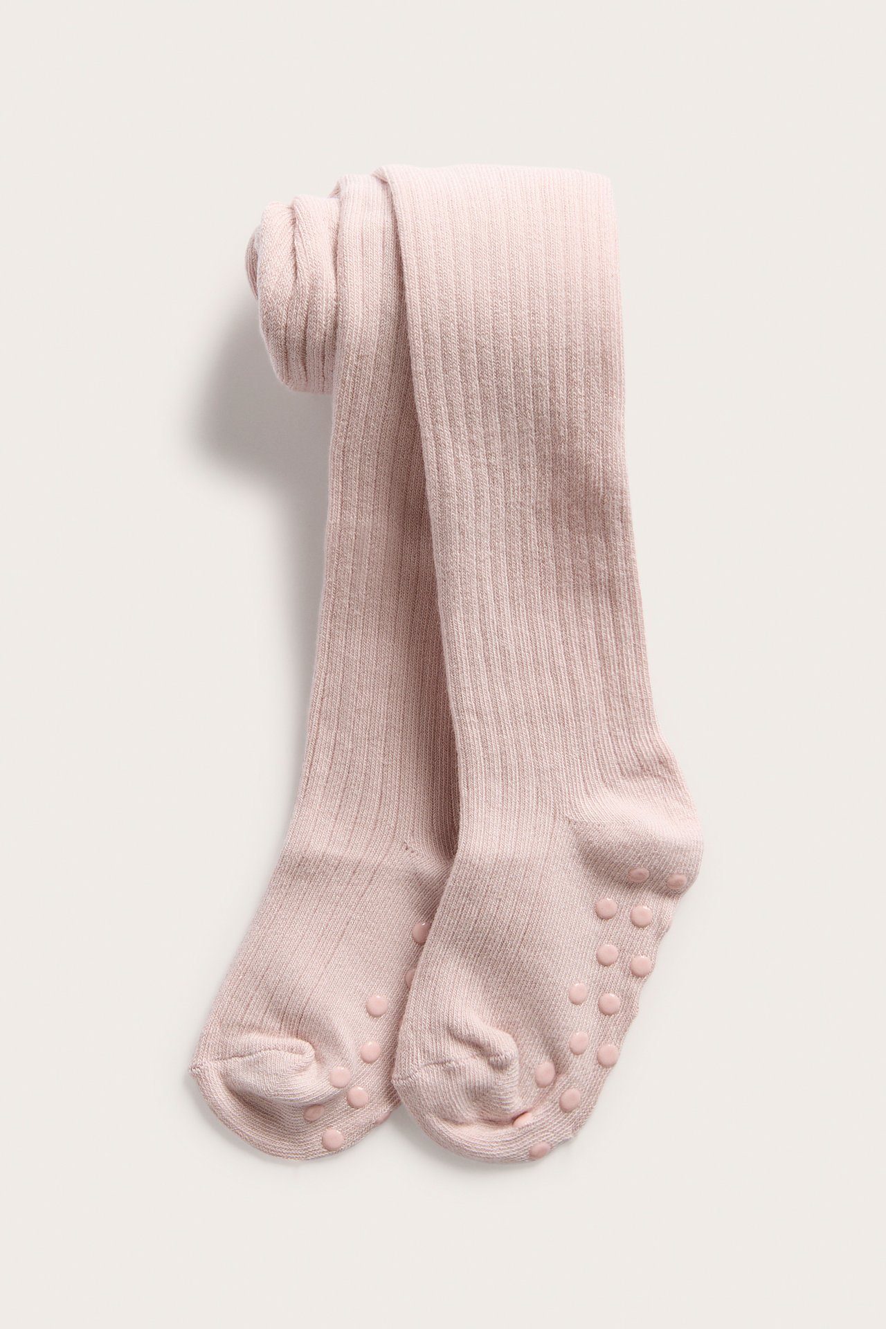 Främre vy av ljusrosa ribbade baby strumpbyxor med antislip-prickar på sulorna.