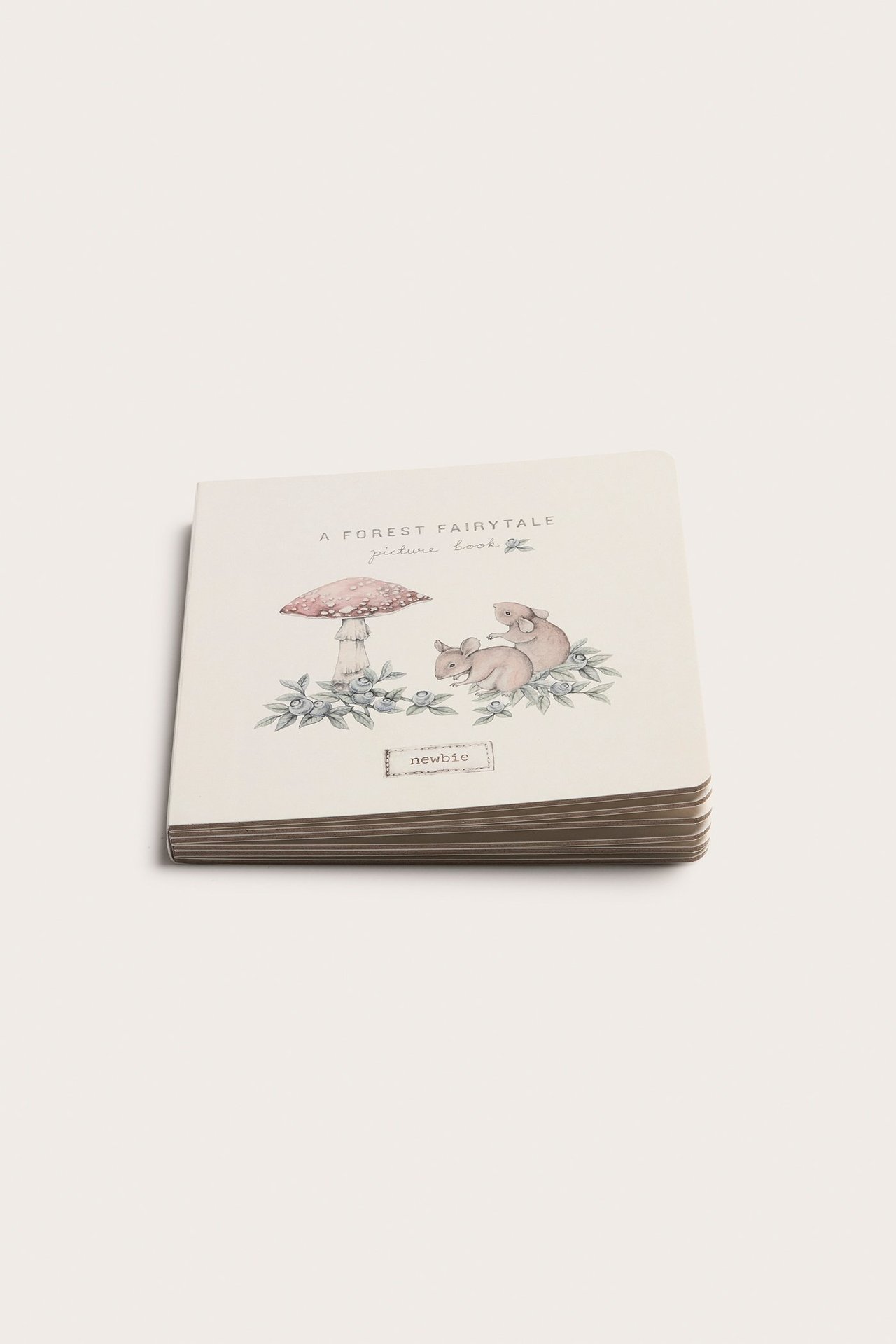 Vinklad framifrånvy av en offwhite mönstrad bildbok med hårt omslag och skogsberättelseillustration.