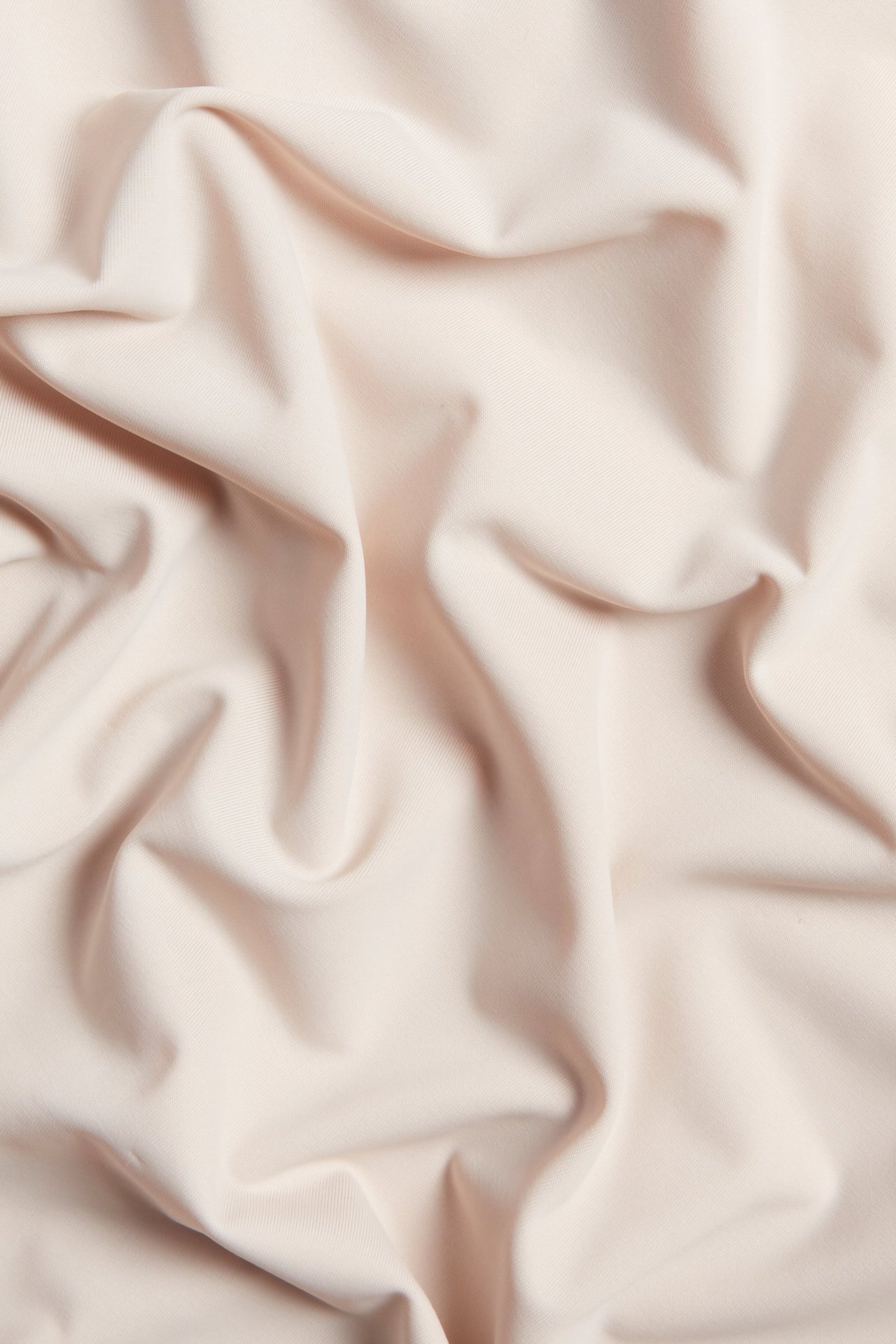 Zbliżenie jasnoróżowego, gładkiego, jednolitego materiału z poliamidu i elastanu na halkę, miękko udrapowanego.