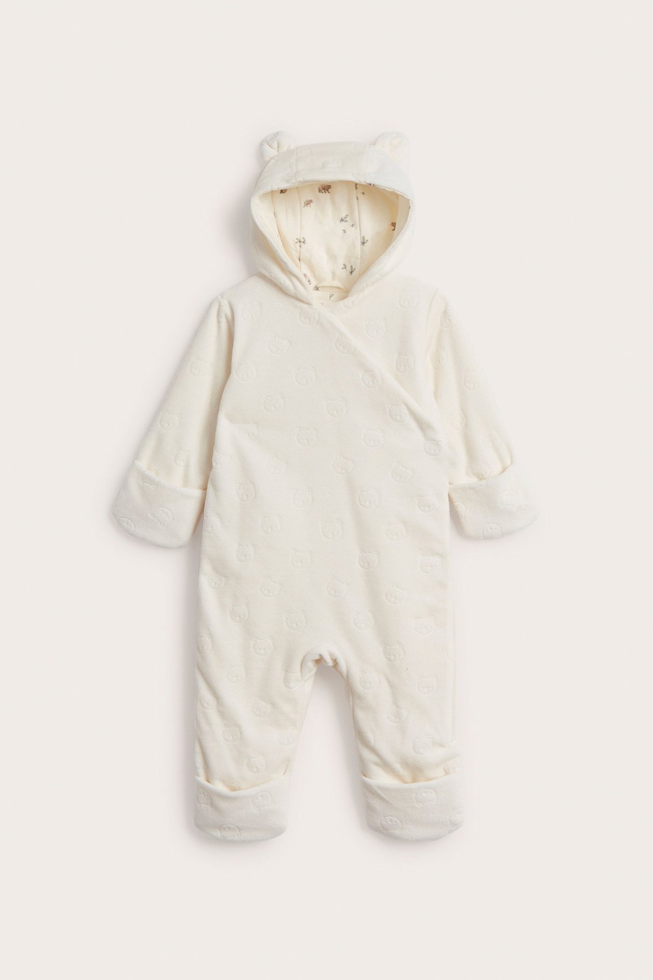 Framsida av en offwhite velouroverall för baby med präglat mönster, huva med öron och tryckt foder.